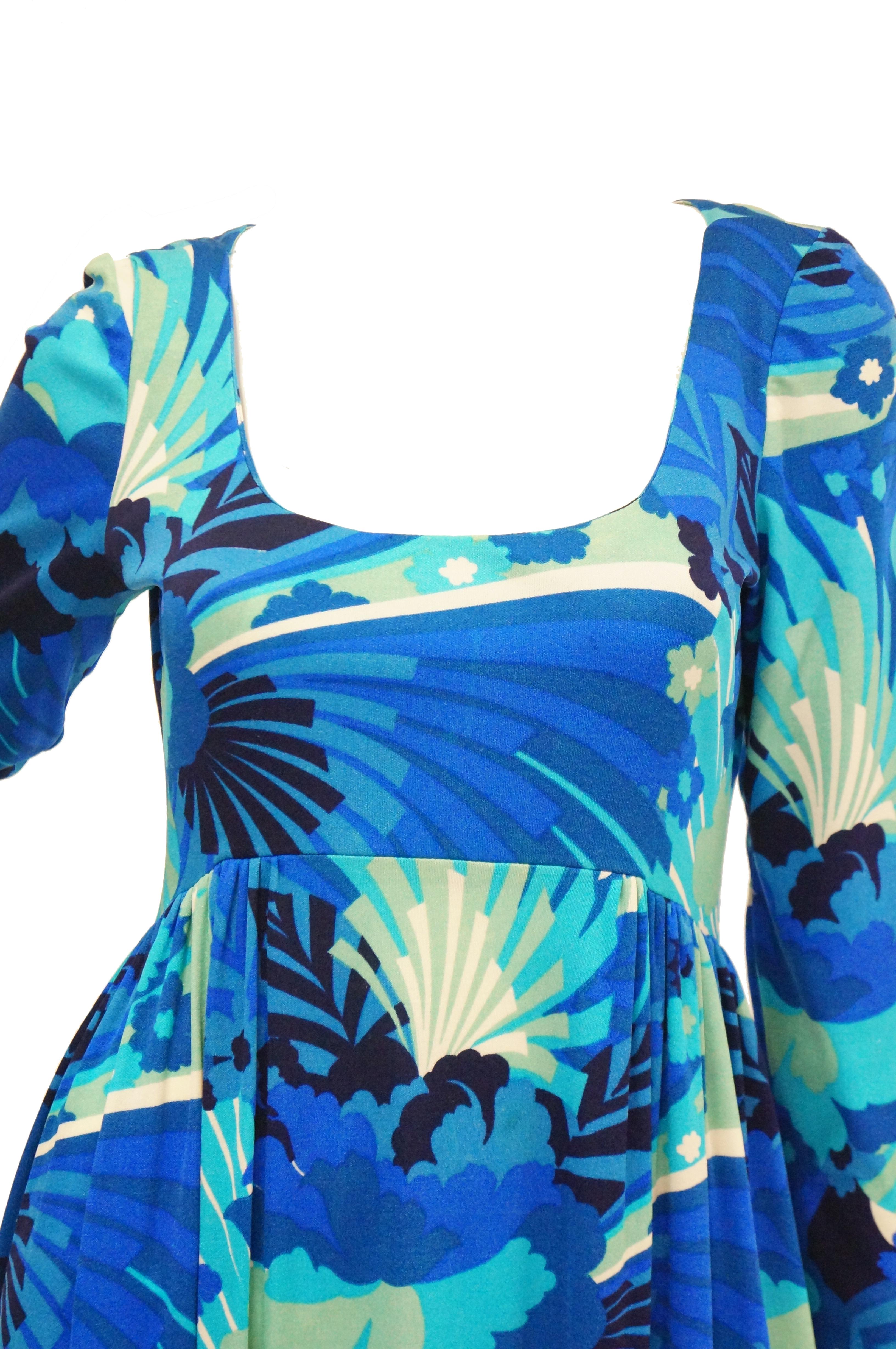 Fabulous and fun blue floral dress by Victor Costa! The dress is maxi length, with long sleeves, a low square neckline, and a high cinched waist that borders on an empire waist. The dress features a pattern in navy, royal, and sky blue, mint green,