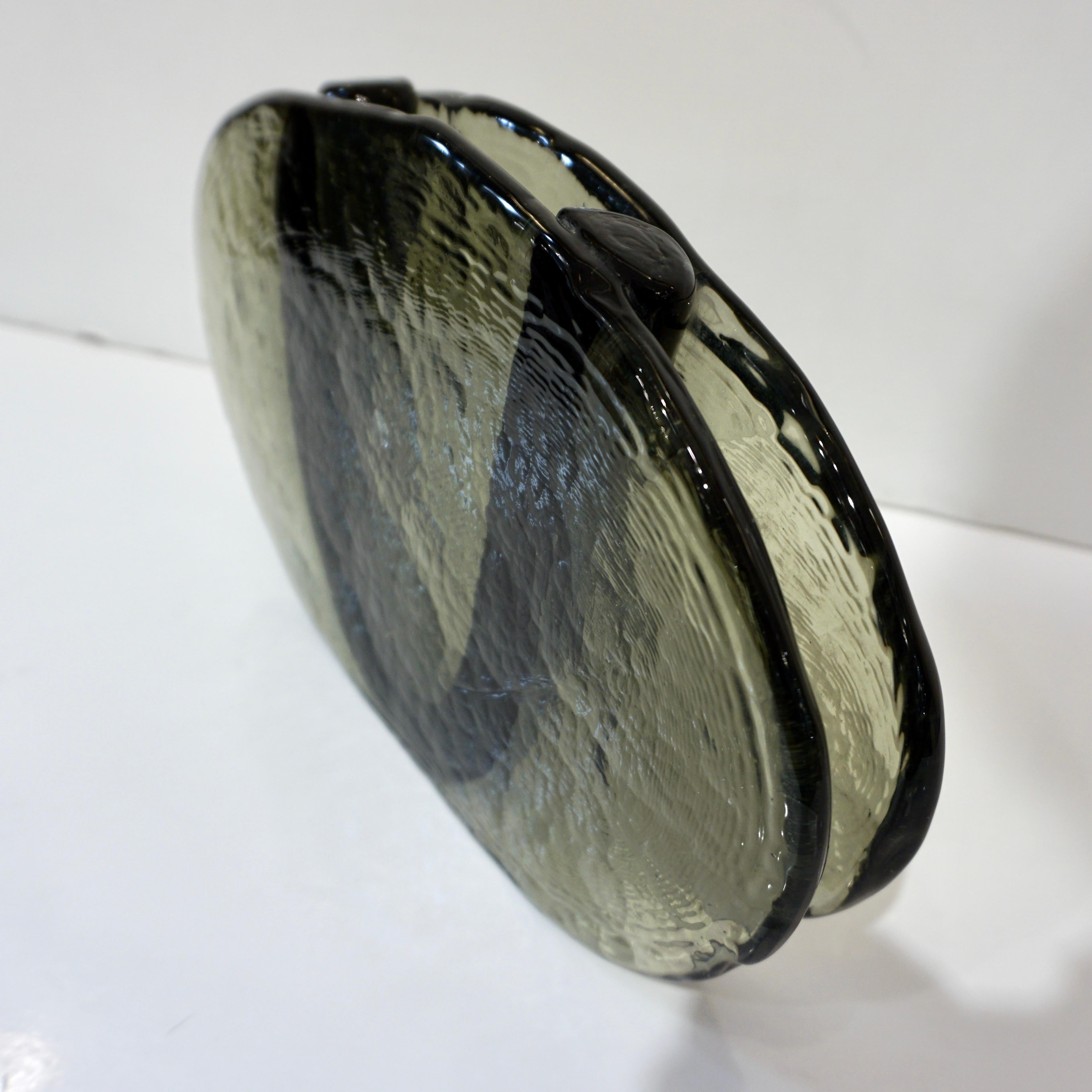A minimalist 1970s vase flower in blown smoked green Murano glass, with a slight hammered texture, a very innovative modern design in oval shape, the central part for the flowers is embraced by a black solid glass U while the sides are open and
