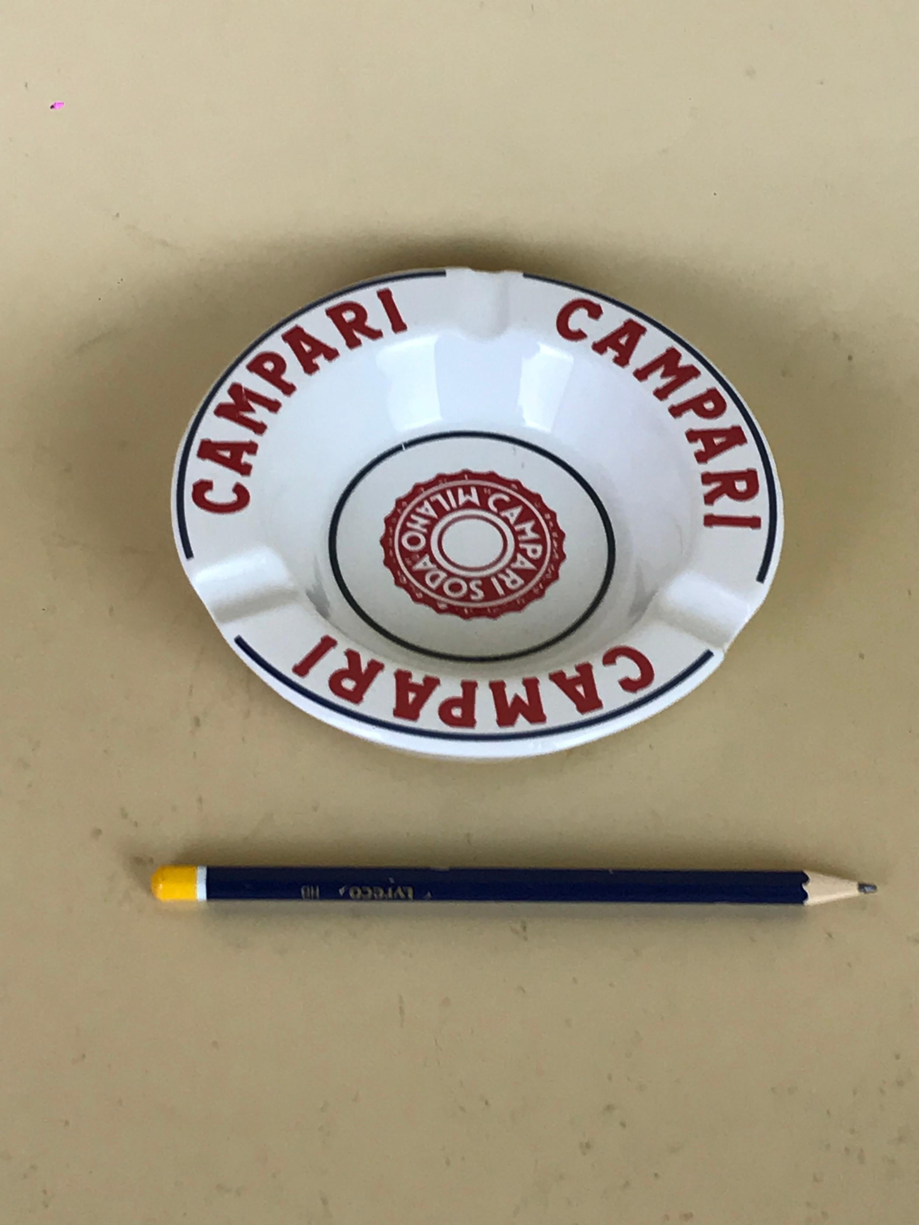 Vintage Campari Soda Milano advertising ashtray in white and red and dark blue ceramic made in Italy by Ceramica E Piola in Carpignano Sesia, Novara in the 1960.

The ashtray is decorated with three Campari logos in red on the border, dark blue