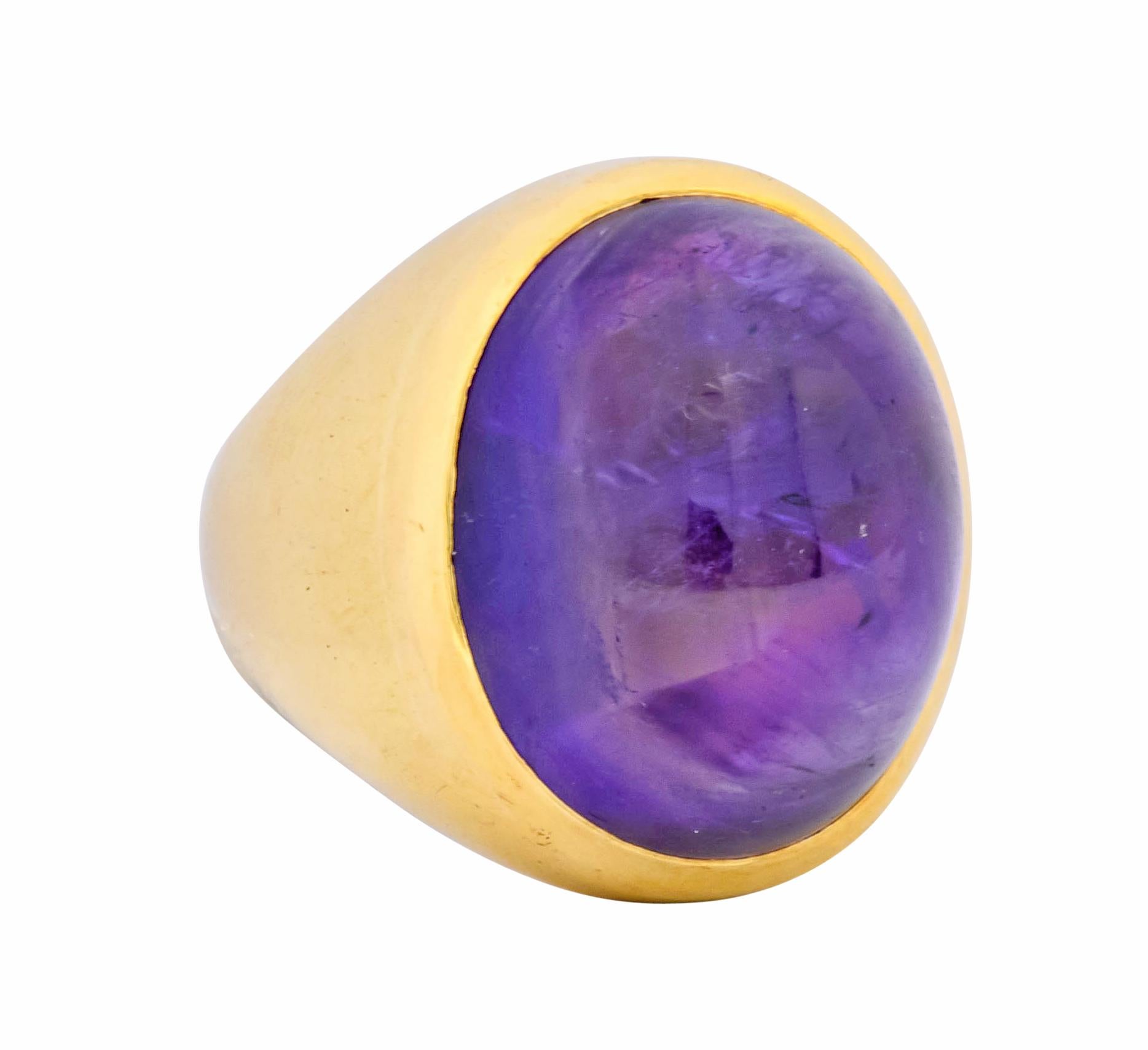 Centering an oval amethyst cabochon measuring approximately 19.2 x 16.0 mm, translucent purple with incredible natural inclusions

Bezel set in a polished gold surround with tapered shoulders

Tested as 18 karat gold

Ring Size: 5 1/2 &