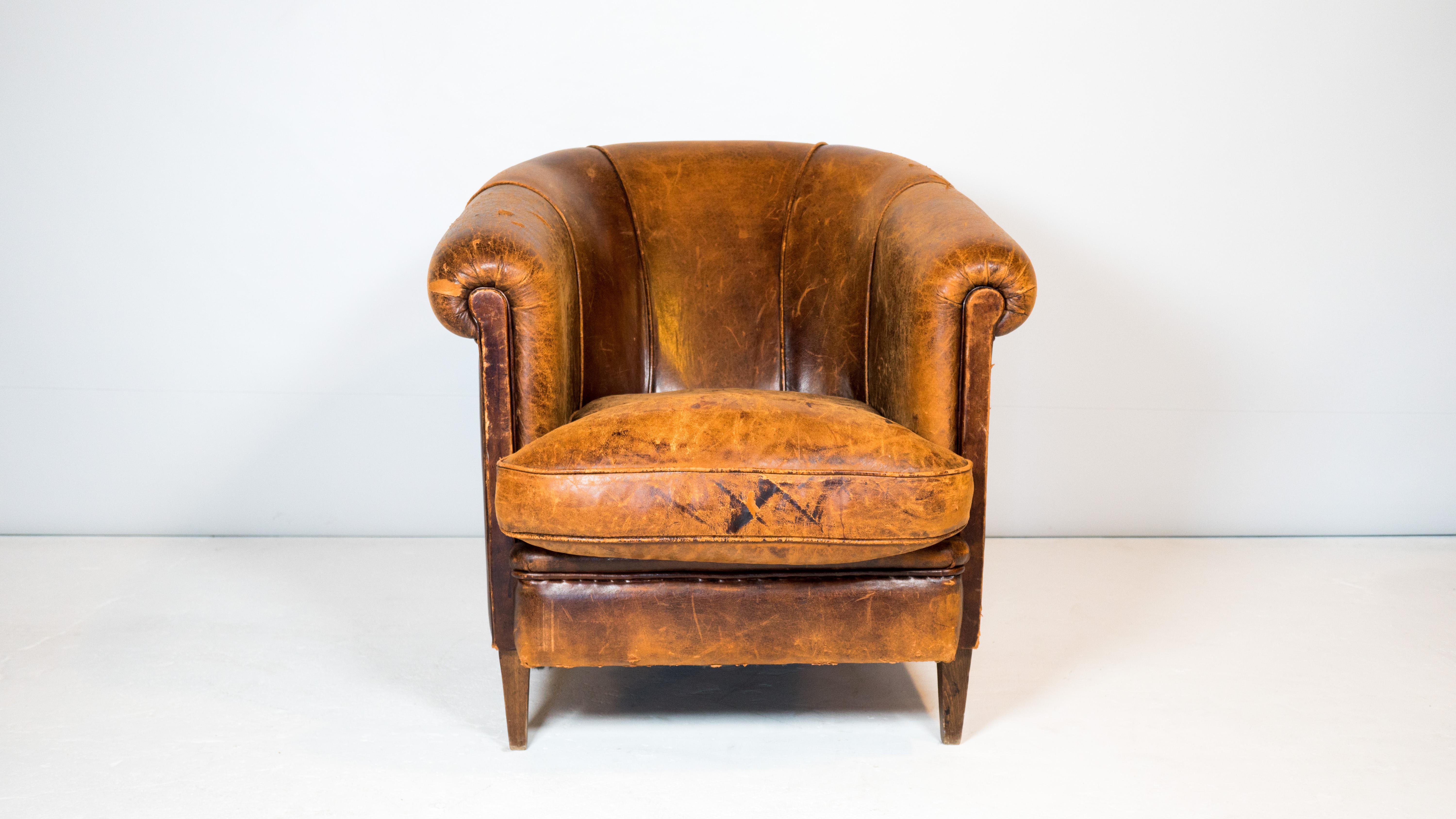 Vintage Art Deco leather club chair, circa 1970s. Beautifully distressed cigar brown leather with aged patina. Rounded armrests that slope around the back for a inviting and lounging feel. Nice stitching details and piping trim. Supported by tapered