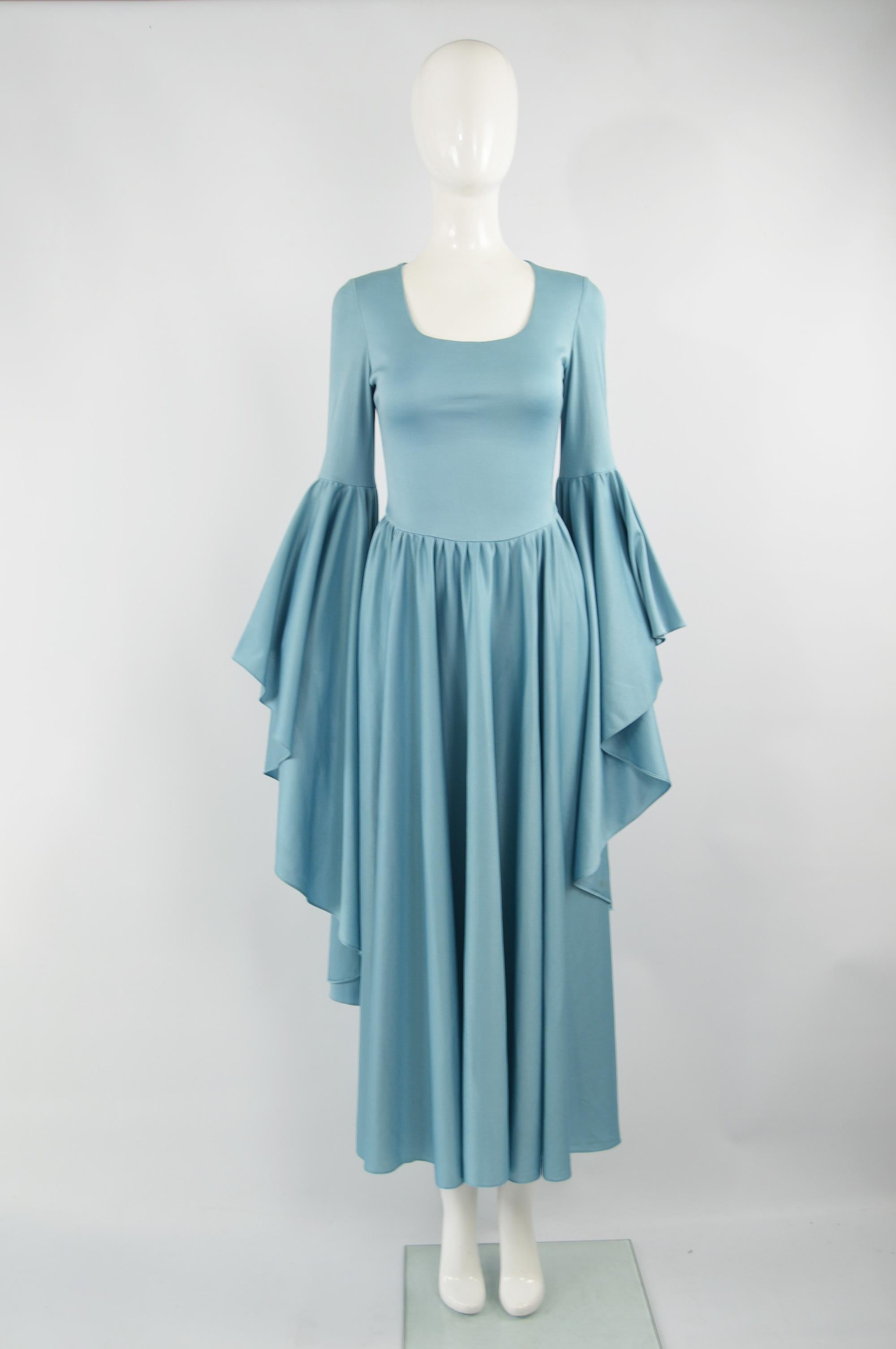 A fabulous vintage evening gown from the 70s by Marisa. In a blue synthetic jersey with a scoop neck, gathers at the waist which give soft pleats in the skirt and huge amazing bell sleeves that make an incredible dramatic statement at any