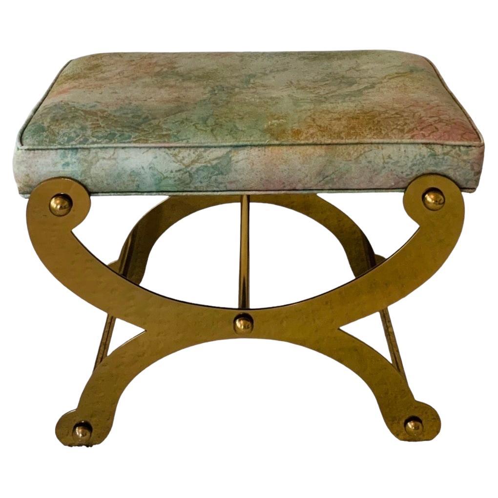 This is a 1970s solid lacquered-brass stool or bench with X-shaped legs and curule details. The silhouette is a modernist iteration of a traditional Empire-style Louis XVI ployant stool. This example's X base is fixed and does not fold, as would a