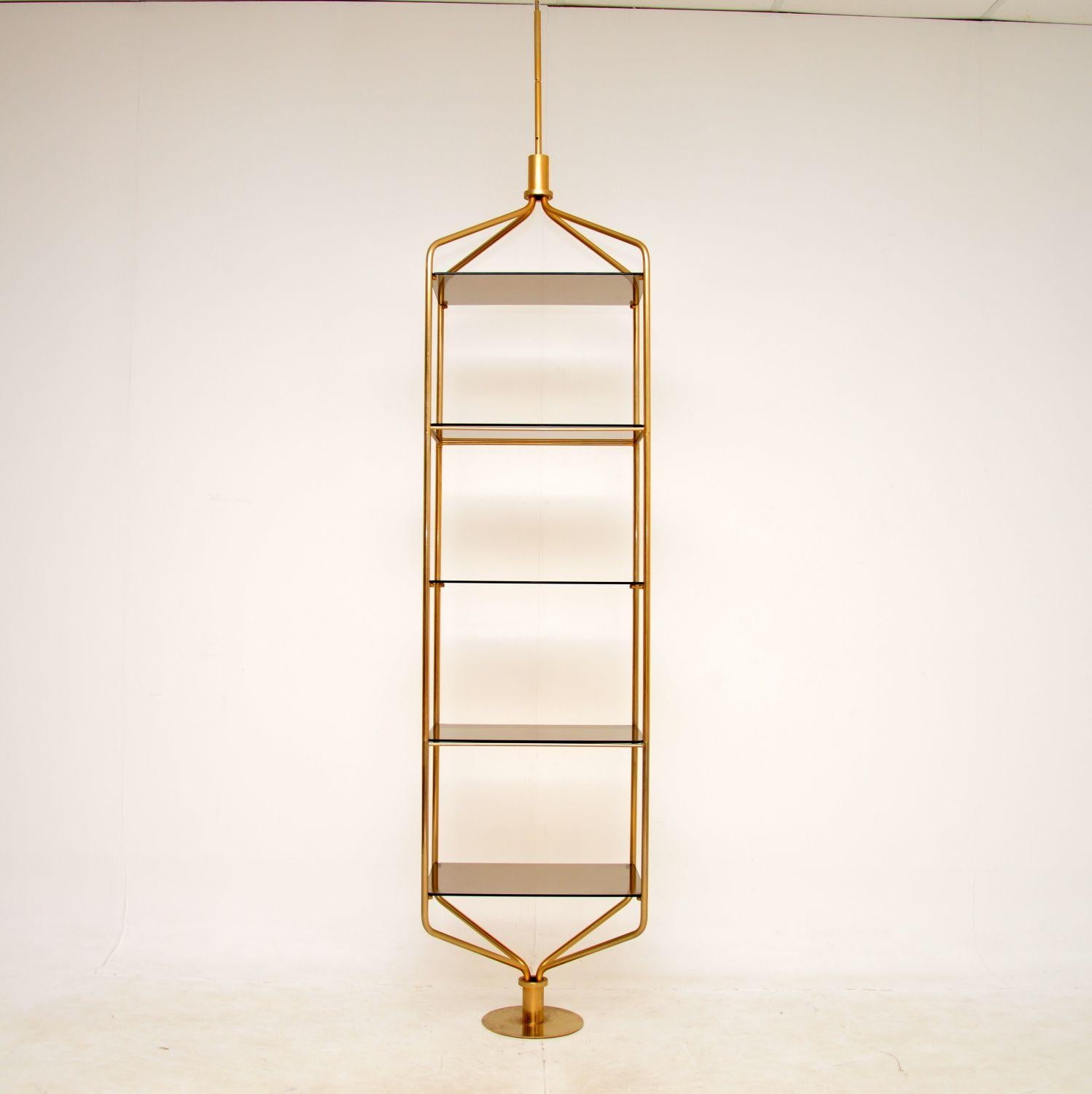 A stunning and very unusual vintage display cabinet in brass and glass. This was likely made in Italy, it dates from the 1970s.

It is beautifully designed, the frame sits on a circular base and has a sharp extension that raises vertically from