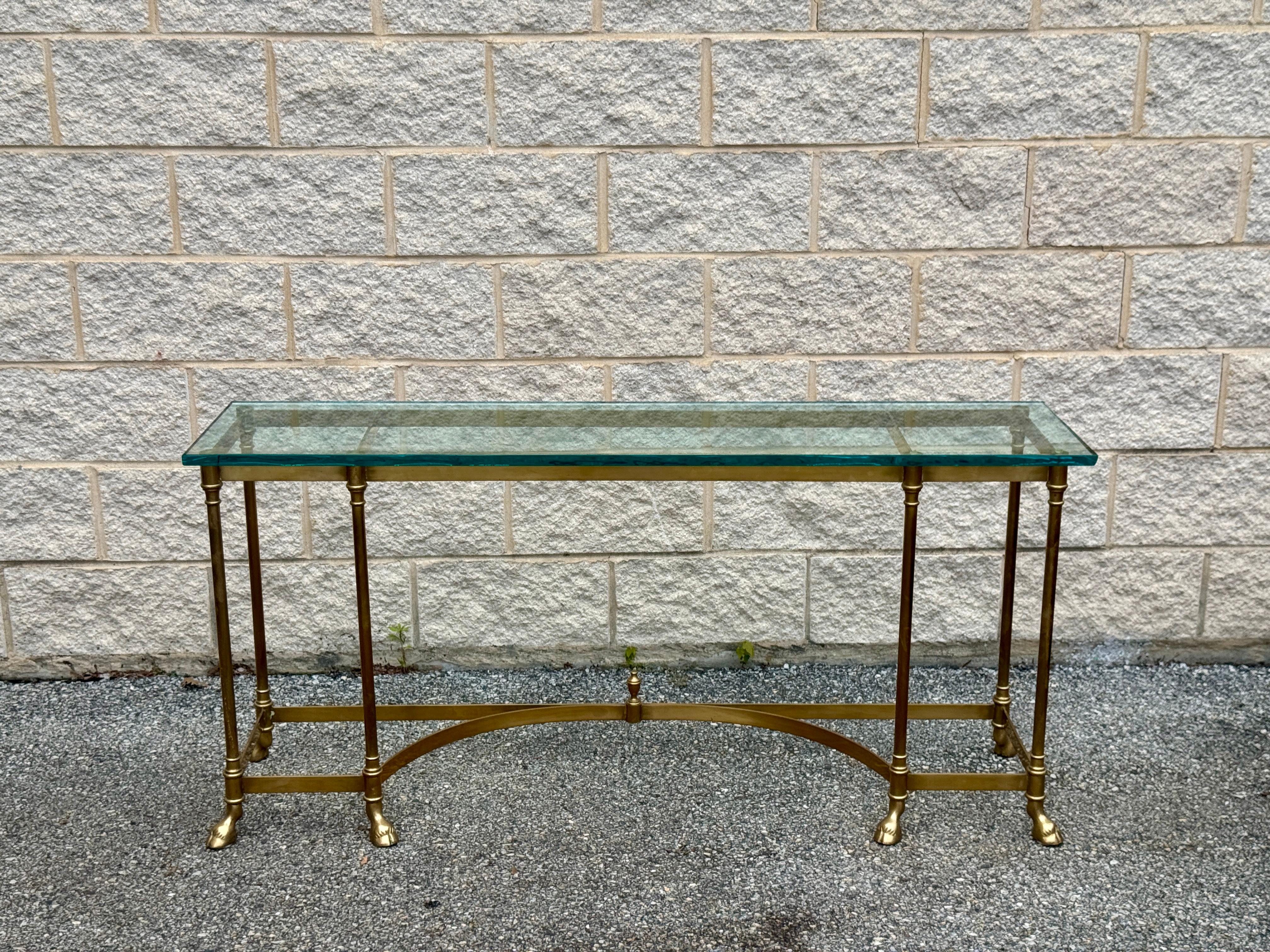 Elegant vintage brass and glass console table featuring a sleek rectangular design with neoclassical influences. The table has a thick beveled glass top supported by fluted brass legs joined by curved stretchers and finished with classic hoof feet.