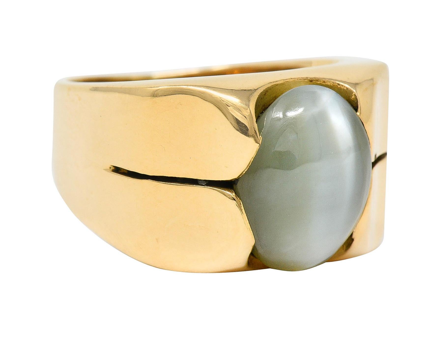Wide band ring features an oval cabochon of cat's eye chrysoberyl

Measuring approximately 12.0 x 9.5 mm

Translucent yellowish green with a sharp to diffused white chatoyant line

Set by stylized wide prongs with subtly split shoulders

Stamped 18K