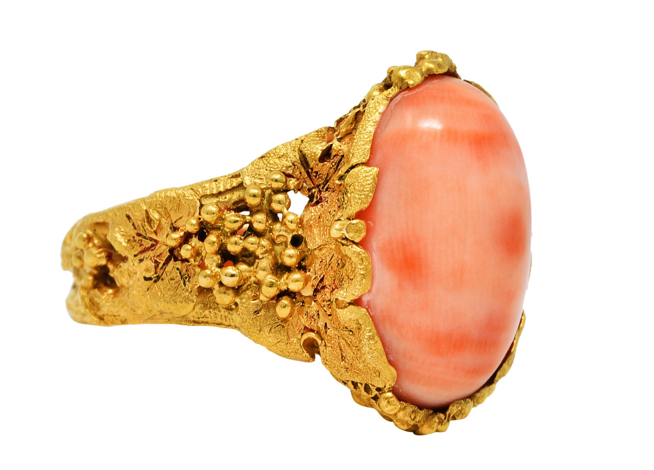 Featuring an oval coral cabochon measuring approximately 16.2 x 10.8 mm

Opaque with pastel peachy pink color swirled with areas of peachy orange

Set in an ornate mounting comprised of grape clusters and vined foliate

Matte gold finish with