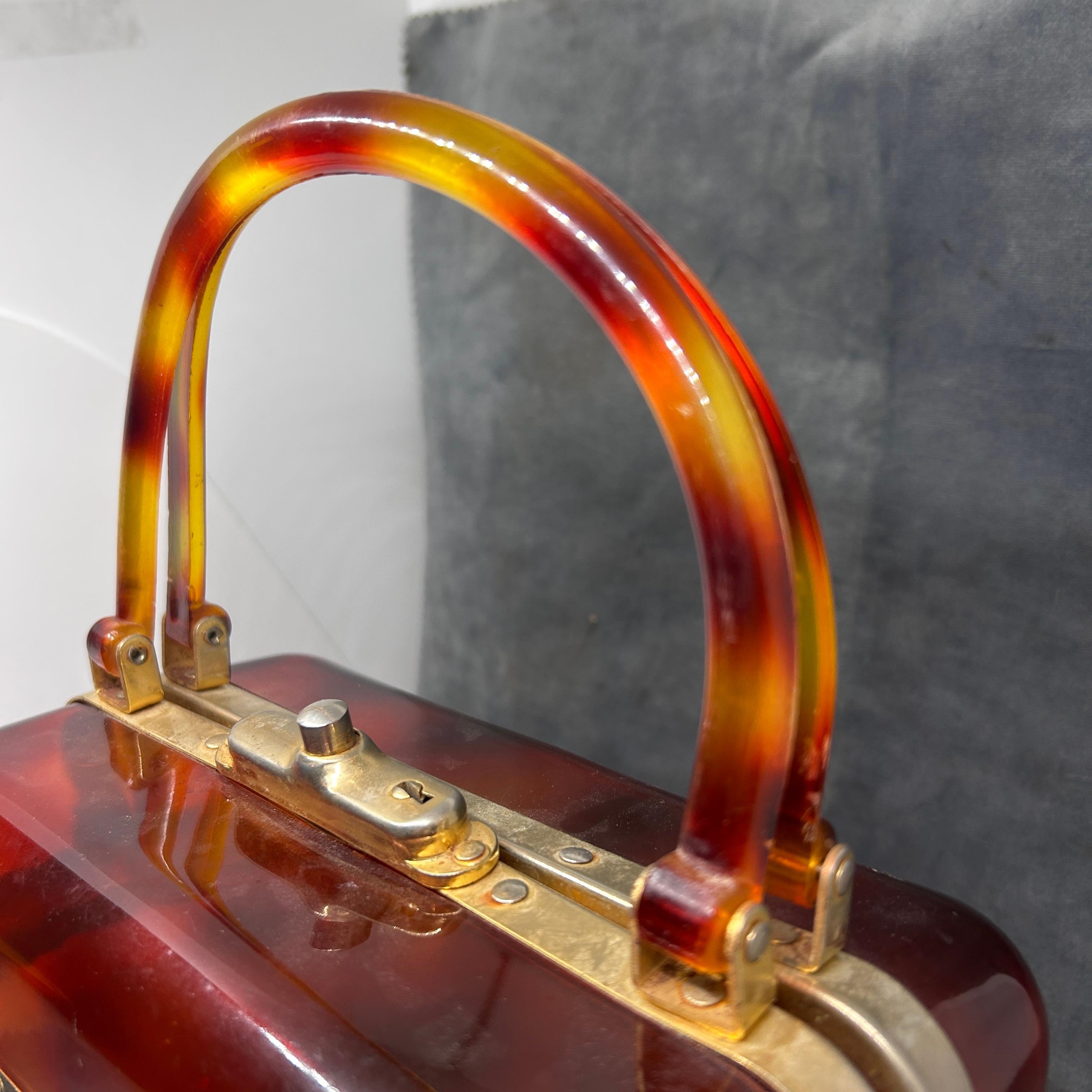 This 1970s Vintage Fake Tortoise Shell Lucite French Handbag is a stunning accessory, notable for its rich faux tortoise shell pattern, structured boxy design, and luxurious gold-tone hardware, all characteristic of the era's stylish yet functional