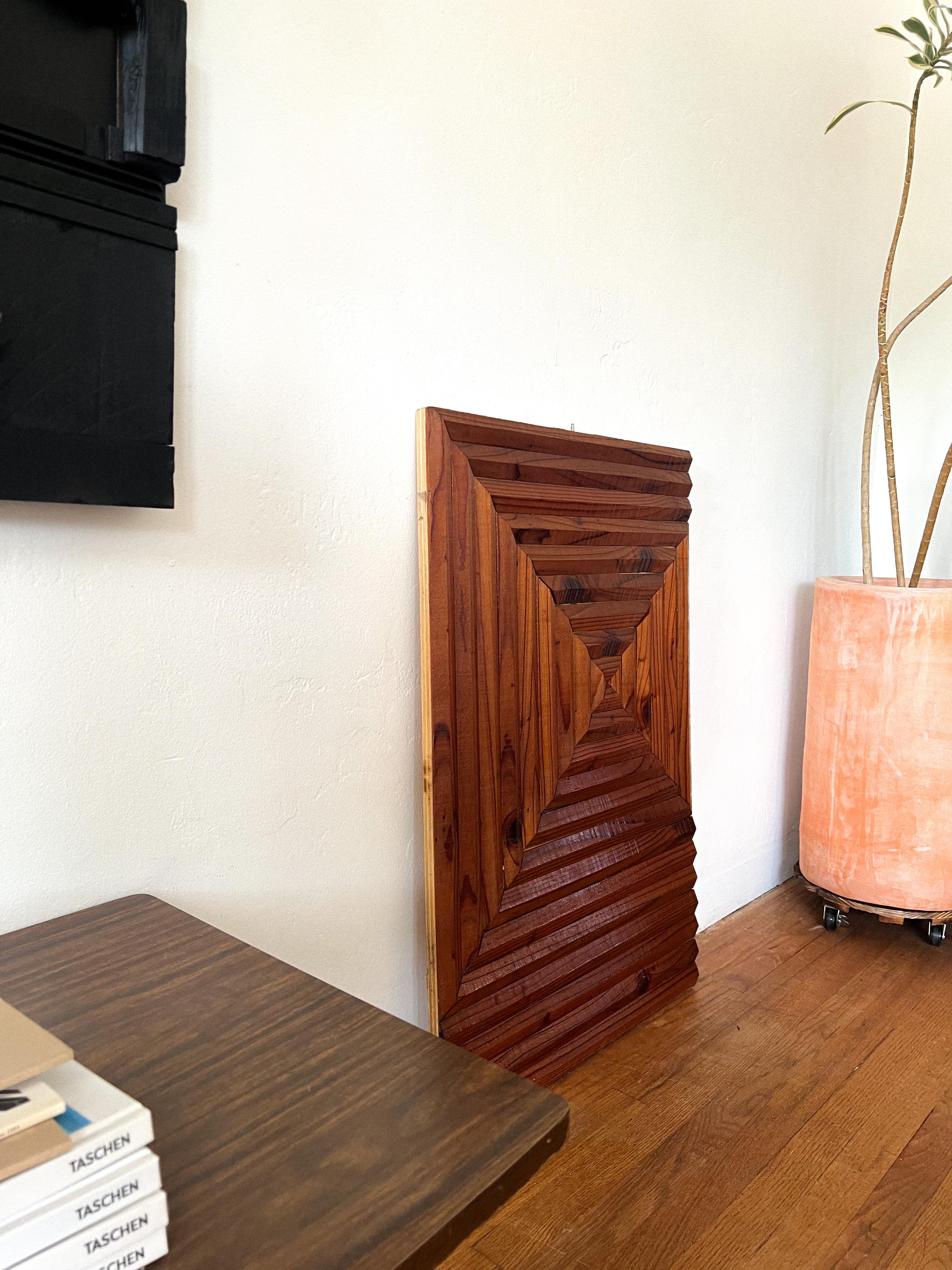 Handcrafted in the 1970s and sourced from a Southern California estate, this sculptural wood wall panel showcases a bold geometric relief design, meticulously assembled from richly grained wood. The pattern radiates from a central point in a dynamic