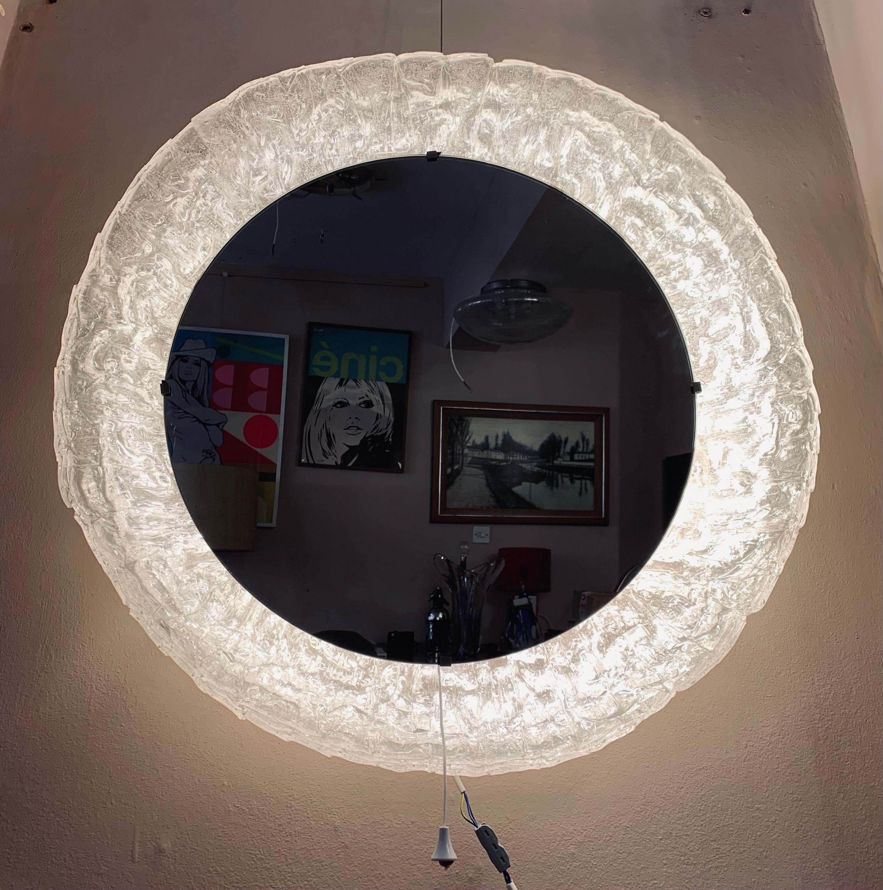 1970s Large German, Hillebrand Lighting, illuminated, backlit, lucite-framed, circular, mirrored-glass wall mirror. The glass mirror is surrounded by a frosted-iced lucite round frame which it hooks onto. This is an unusual version with the mirror