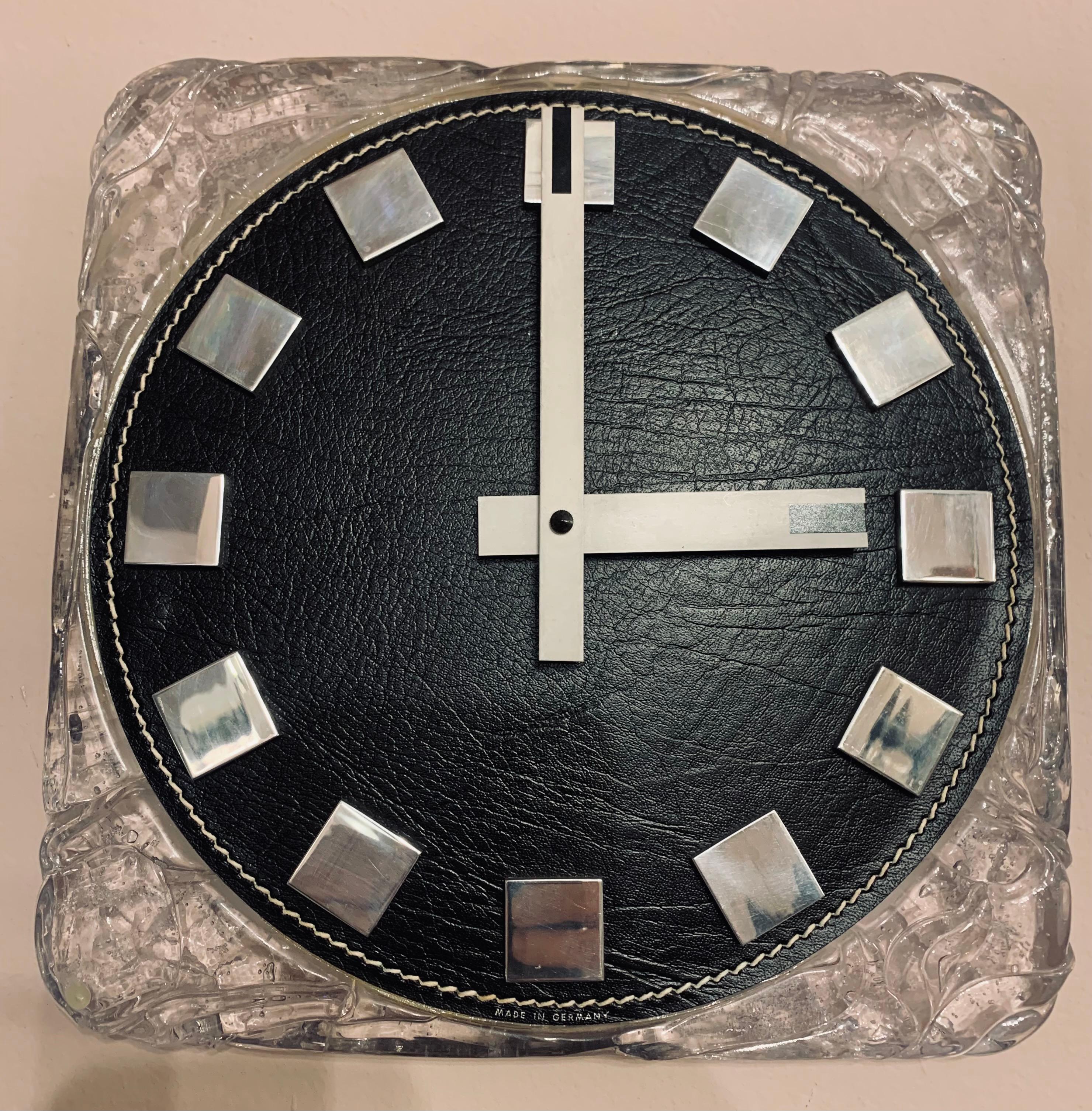 A vintage German wall clock manufactured by Kienzle in the 1970s. The clock features a black leather round clock face with white stitched detail around the circumference. Stainless steel squares designate the hours with contrasting white hour and