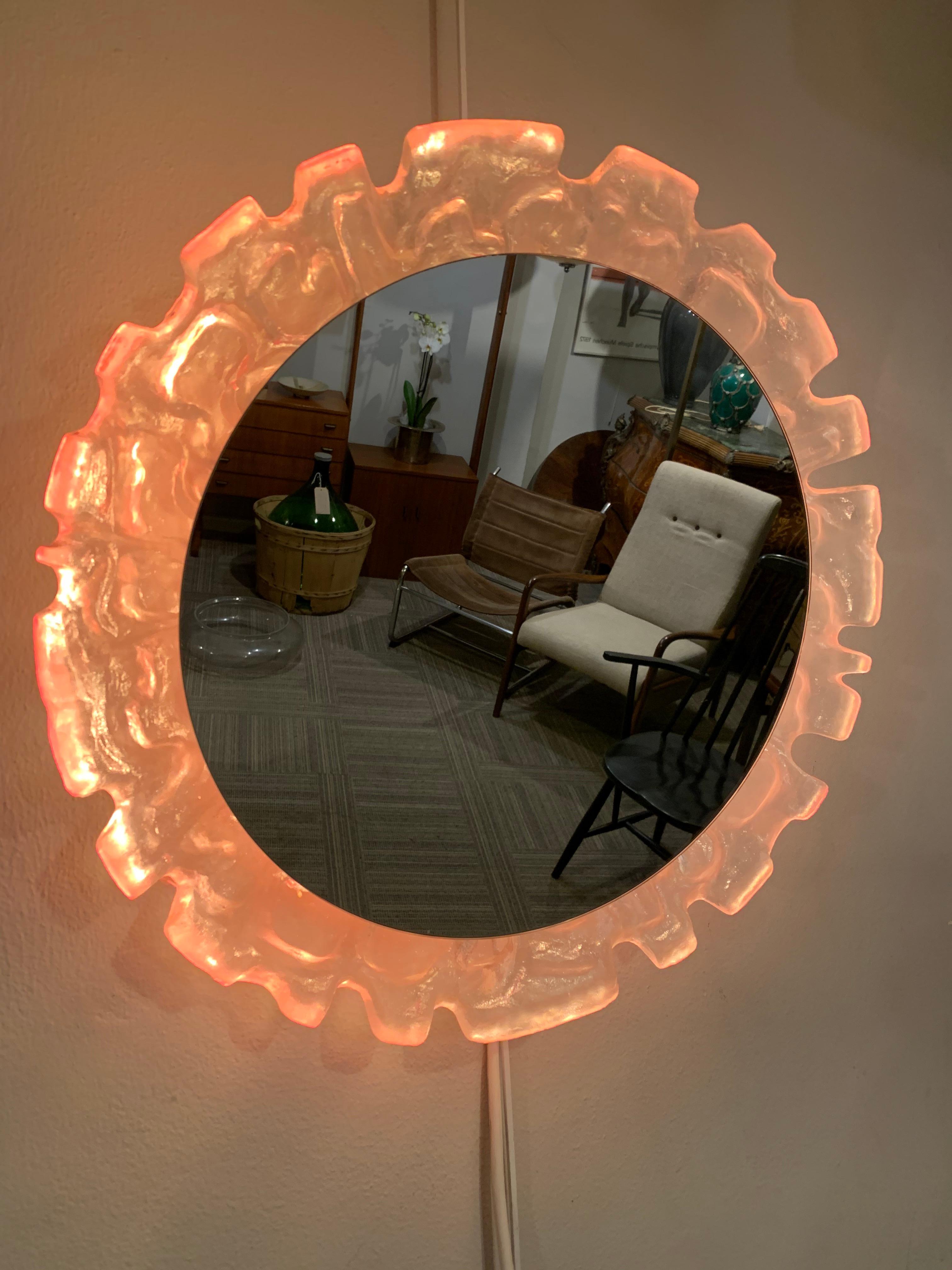 1970s vintage German Lucite illuminated wall mirror manufactured by Erco. The round mirror hangs within an unusual abstract sculpted and textured molded resin surrounded which is backlit. The 4 small E14 screw in 15w pygmy bulbs are surrounded by an