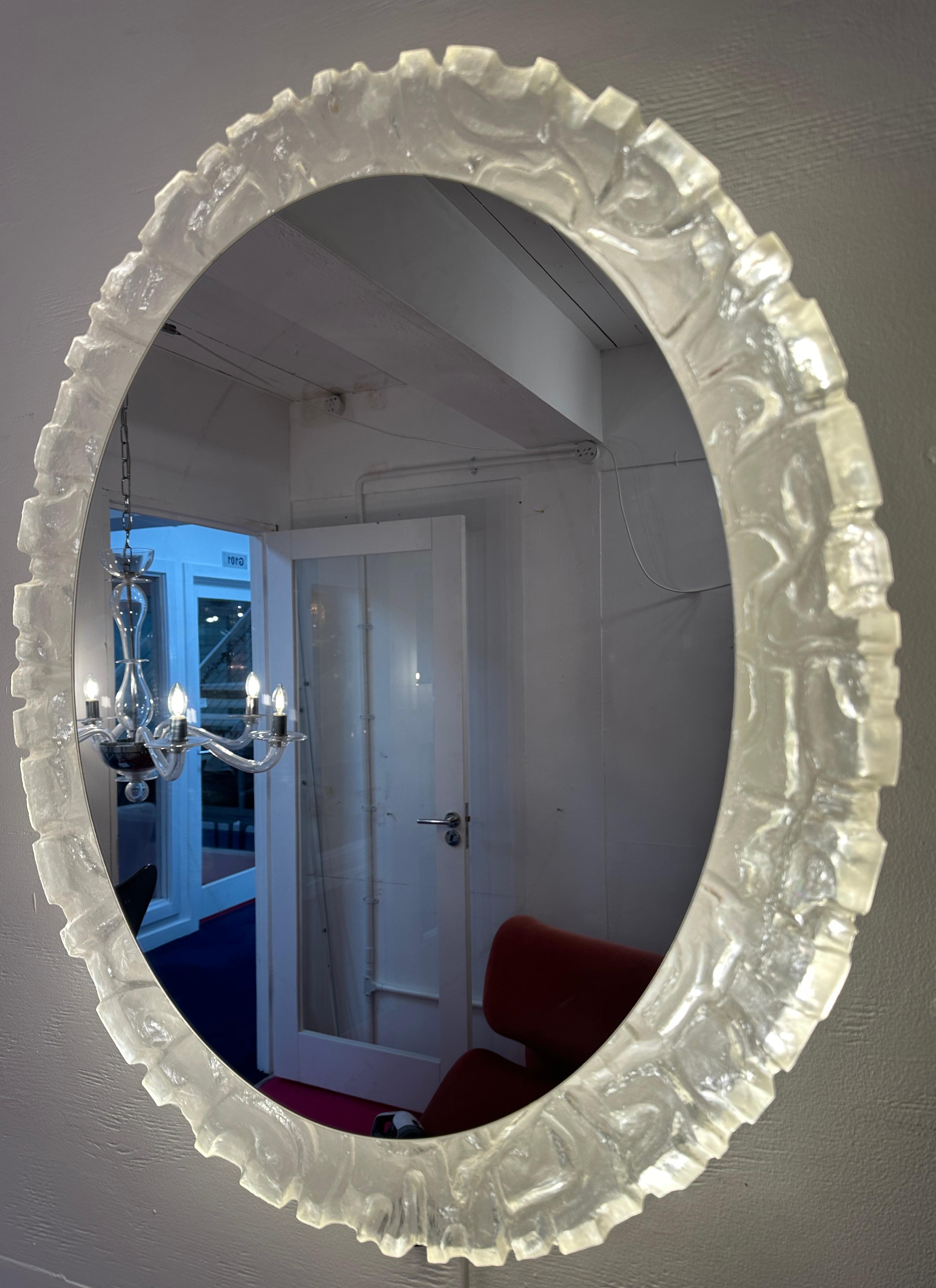 Miroir mural ovale rétro-éclairé vintage allemand en acrylique/lucite. Fabriqué par Erco dans les années 1970.  Le miroir ovale est placé dans un cadre moulé abstrait, sculpté et texturé qui reflète la lumière de manière uniforme, donnant une lueur