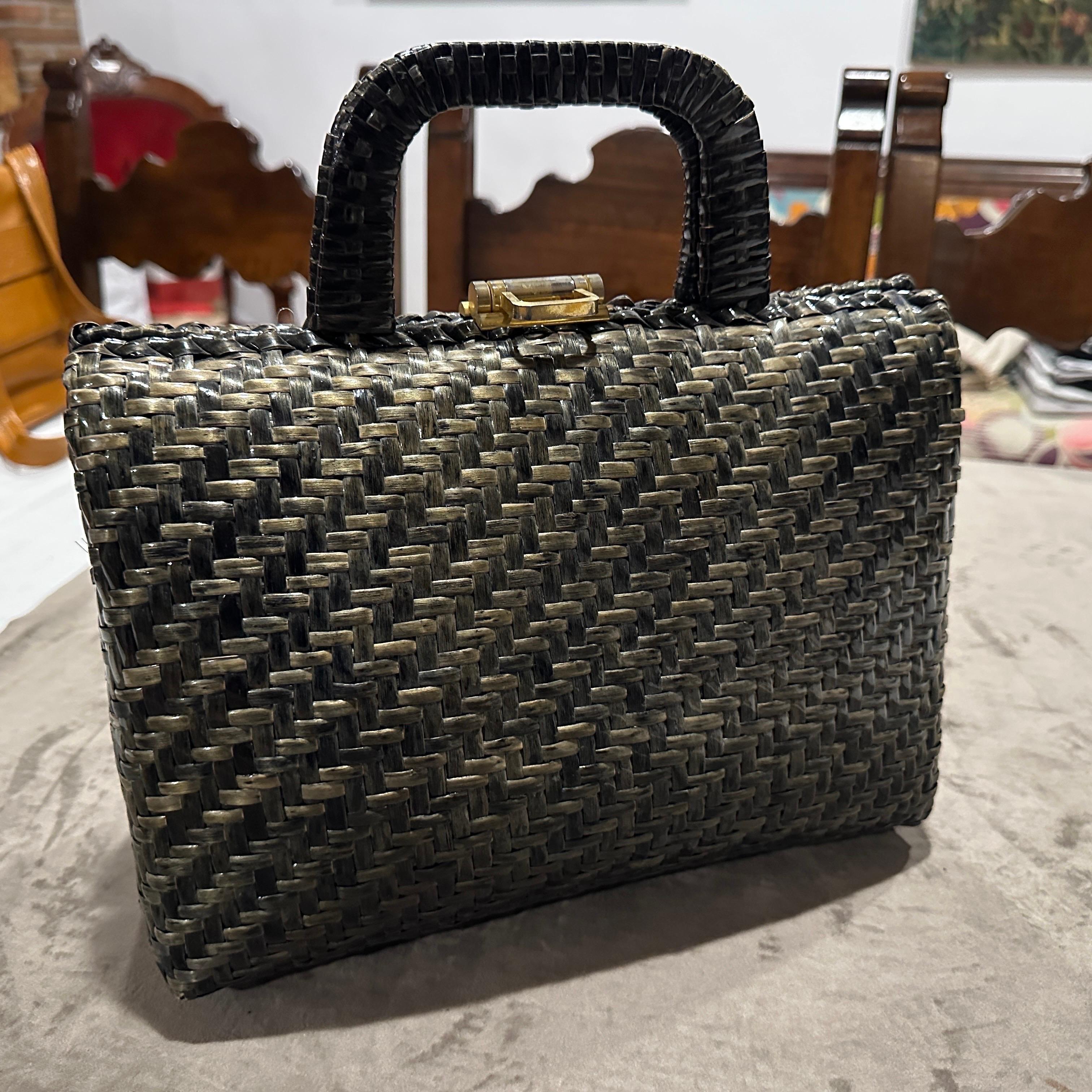 Questa borsa italiana vintage degli anni '70 è caratterizzata da una sorprendente combinazione di vimini intrecciati verdi e neri, che creano un design strutturato ed elegante. La borsa è strutturata con una forma rettangolare, tipica dell'epoca, e