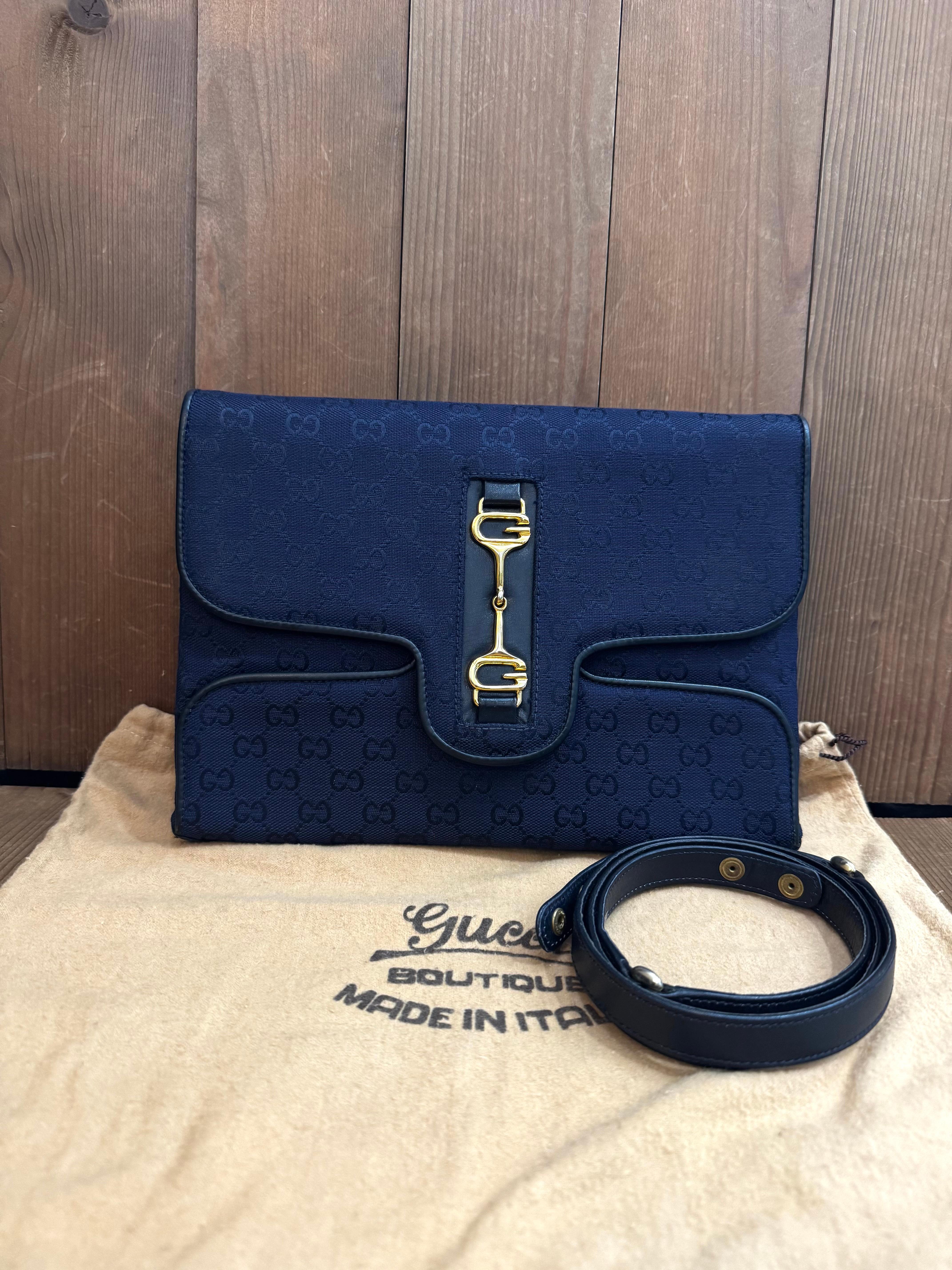 This Vintage GUCCI Boutique 2-way clutch/shoulder bag is crafted of GG monogram jacquard in navy trimmed with smooth navy calfskin leather featuring an interlocking GG horsebit on the front. Front flap snap closure opens to a leather interior