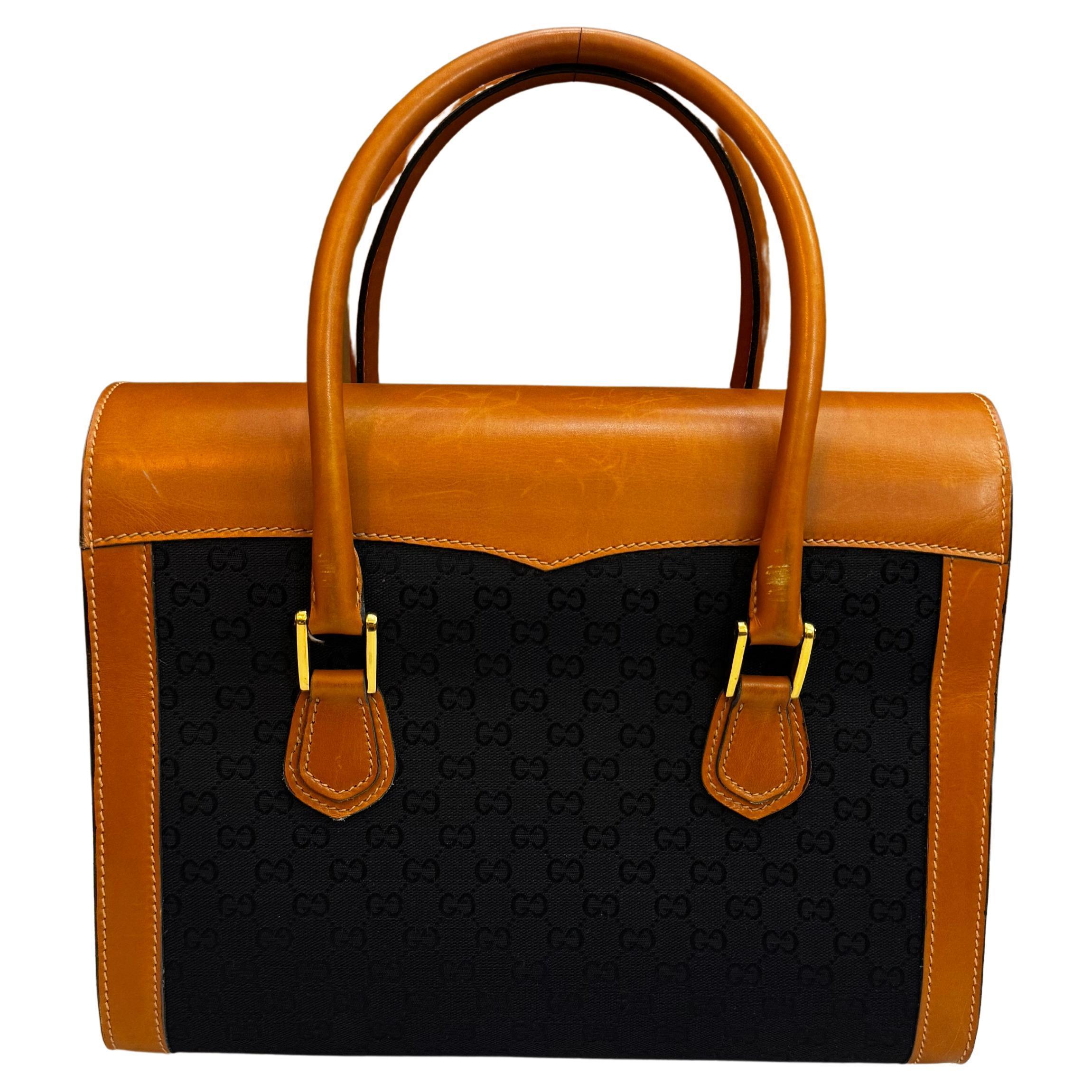 Este bolso vintage Gucci Boston está confeccionado en jacquard negro con el monograma GG, ribeteado en piel de becerro lisa marrón, con asas enrolladas de piel y herrajes dorados. La solapa frontal con cierre de hebilla se abre a un interior de piel