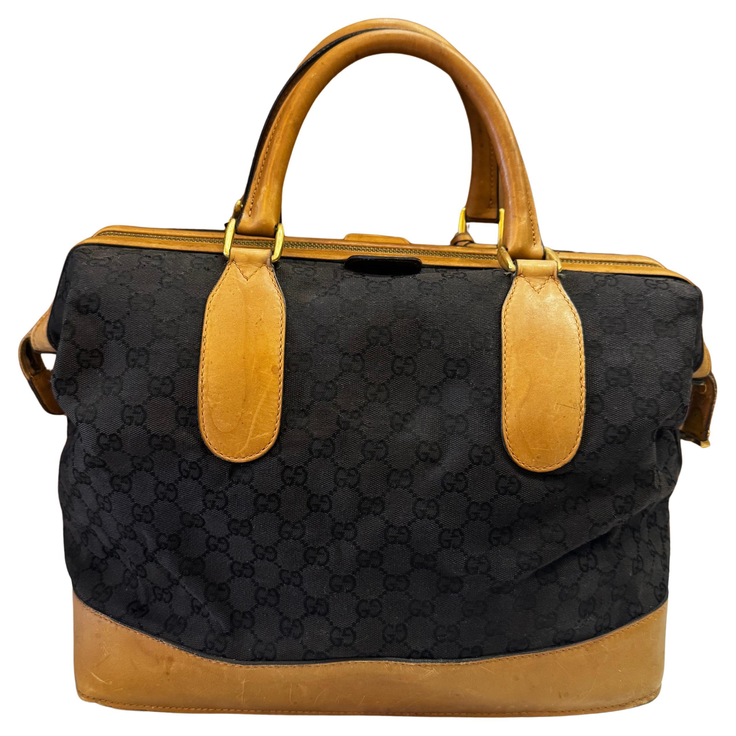 Este bolso doctor vintage de Gucci está confeccionado en jacquard negro con el monograma GG, ribeteado en piel de ternero lisa marrón, con asas enrolladas de piel y herrajes dorados. La cremallera superior con cierre a presión se abre a un interior