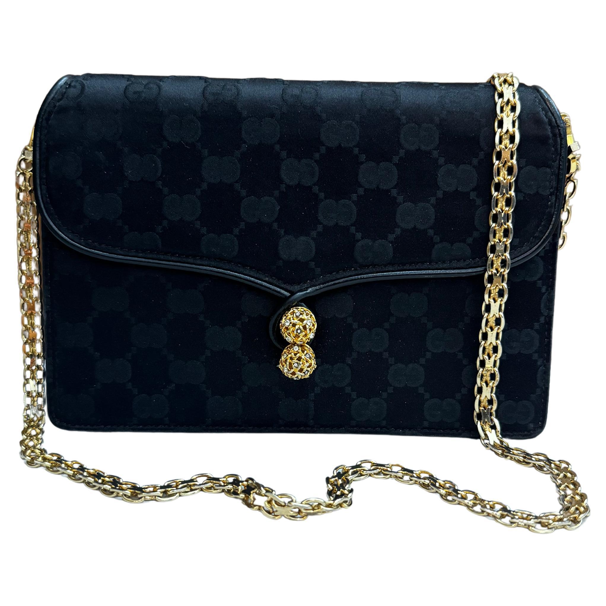 This vintage GUCCI two-way chain clutch shoulder bag is crafted of GG satin jacquard in black featuring gold toned hardware. Front flap closure opens to a silk interior in beige featuring patch pockets and a zippered pocket. This vintage Gucci also