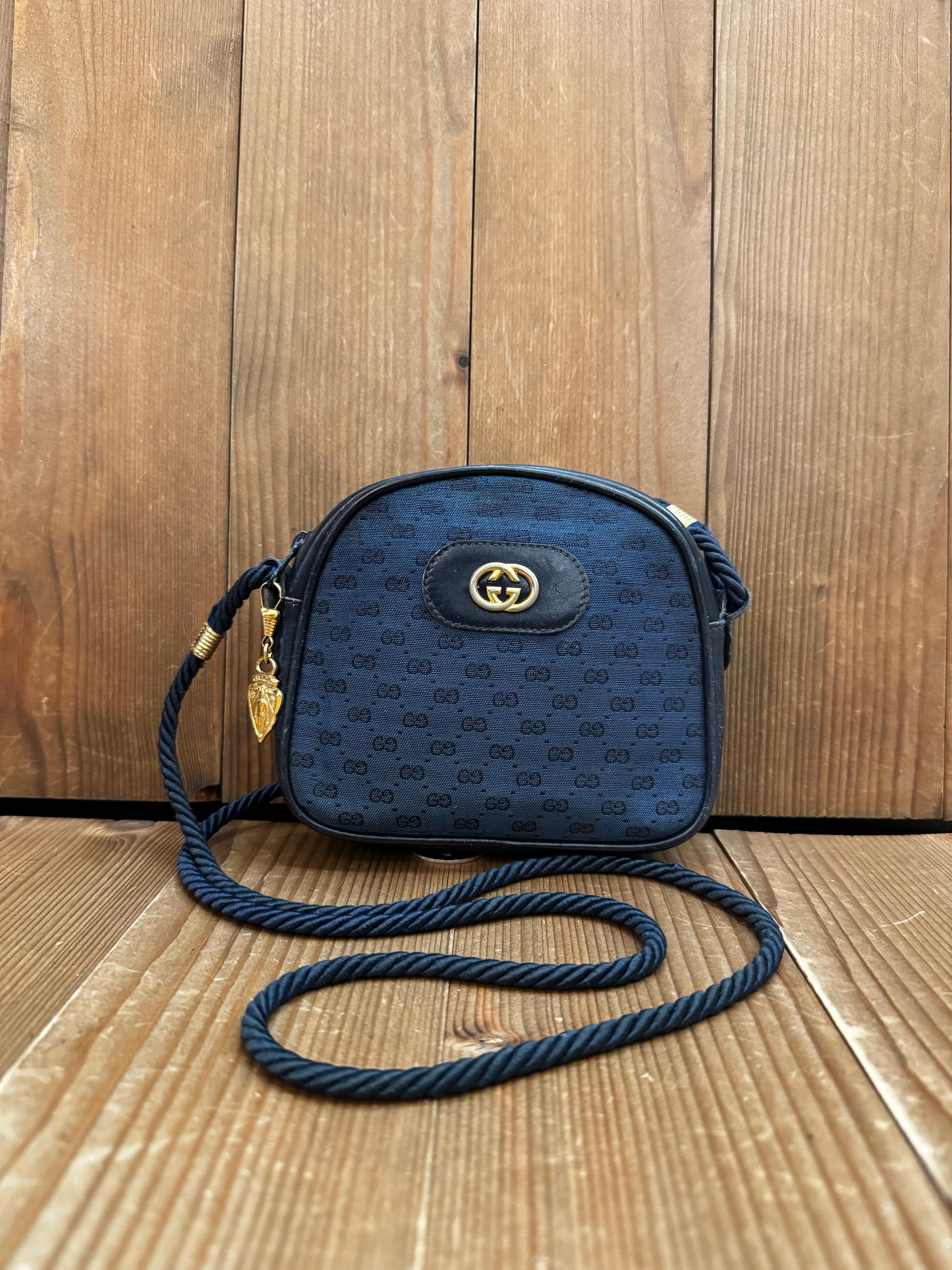 This vintage GUCCI micro crossbody bag is crafted of micro CC jacquard in navy featuring gold toned hardware and a rope strap. Top zipper closure opens to a leather interior in black. Made in Italy. Measures approximately 5.75 x 5 x 1.5 inches Strap