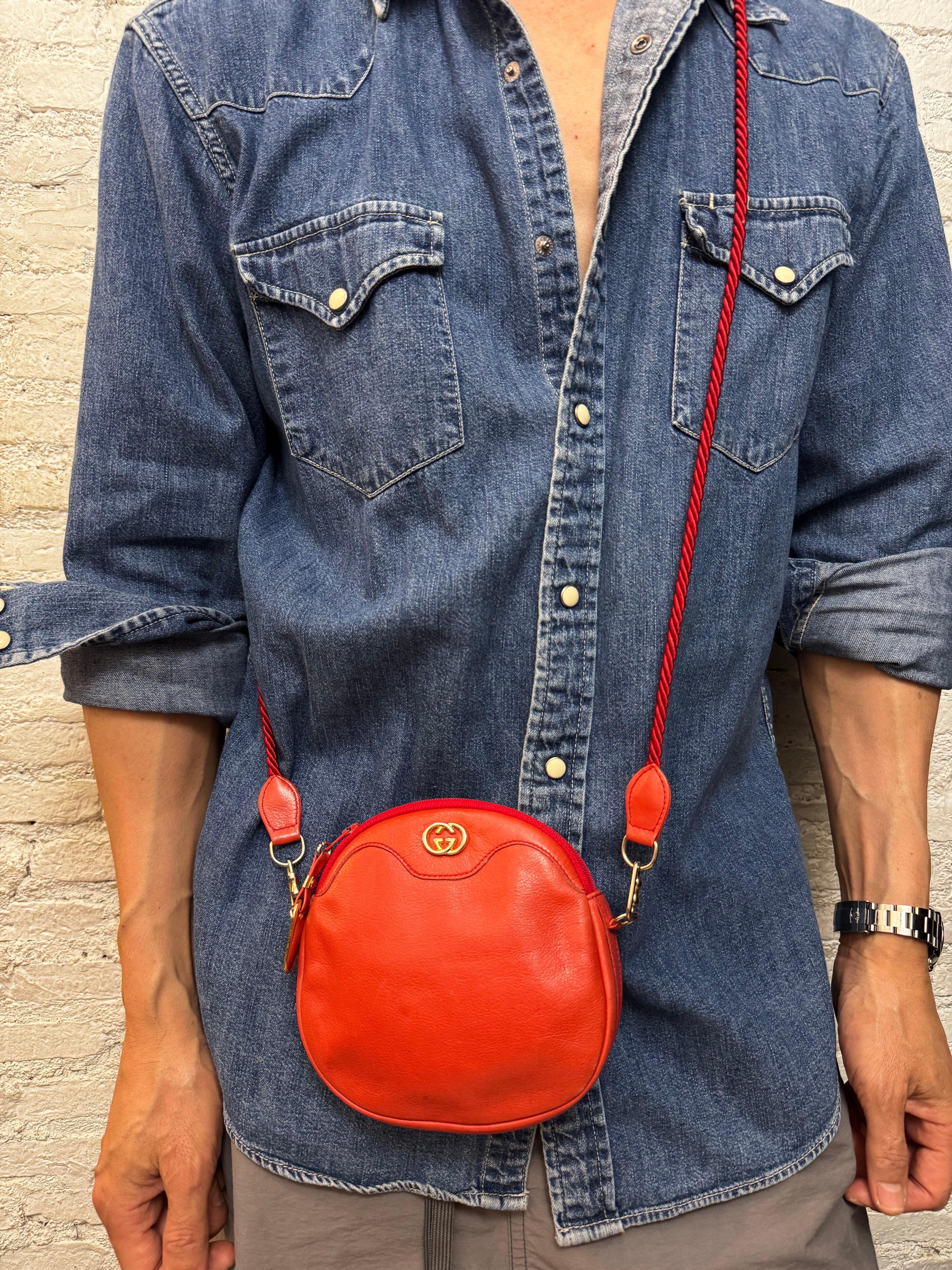 Este micro bolso cruzado vintage GUCCI está confeccionado en piel de becerro de grano pequeño de color rojo, con herrajes dorados y una correa desmontable de cuerda de seda. El cierre de cremallera superior se abre a un interior de piel beige.