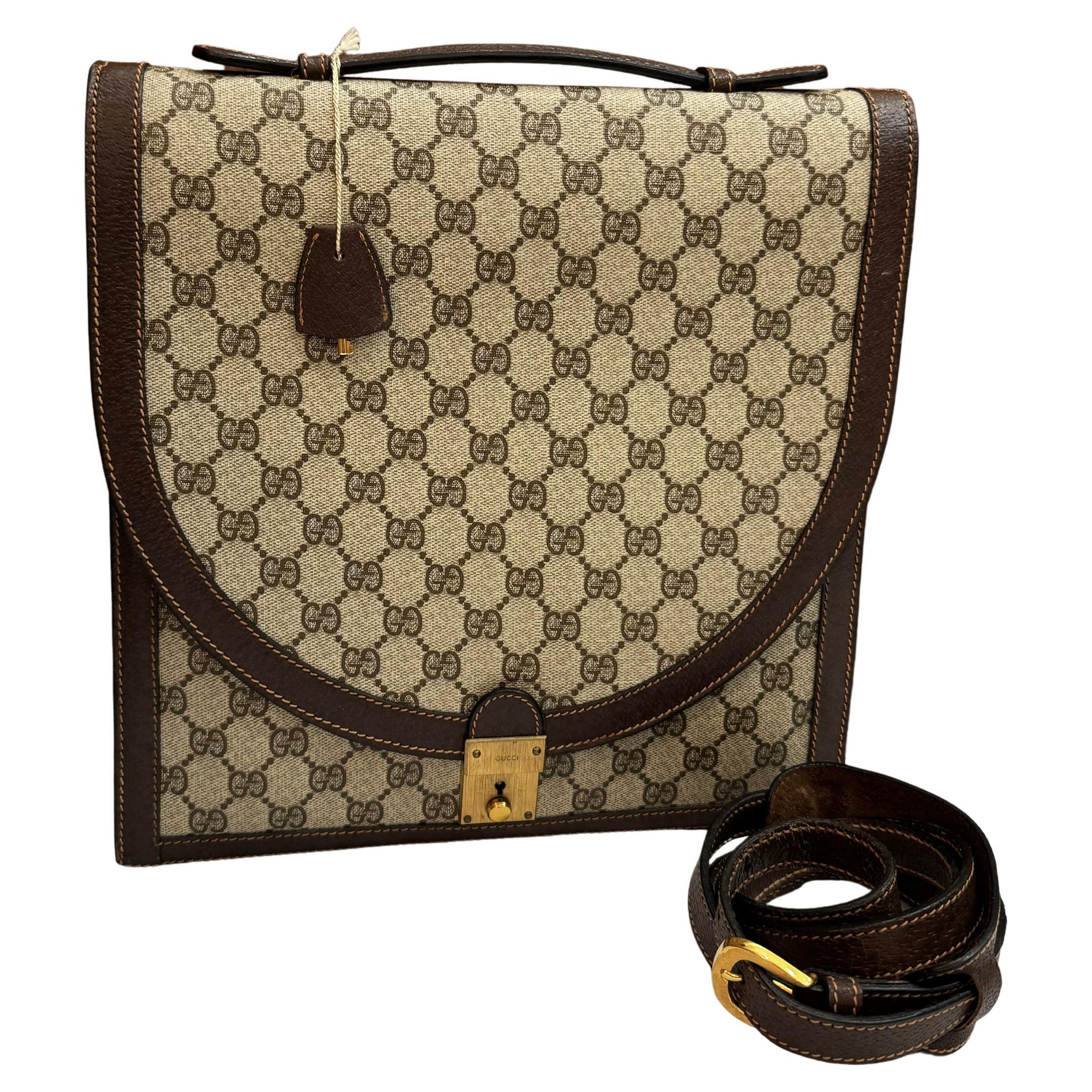 Este bolso portadocumentos vintage GUCCI de dos compartimentos está confeccionado en lona revestida con el monograma GG y piel de cerdo en marrón, con herrajes de latón dorado y una correa para el hombro desmontable de la misma piel. La solapa