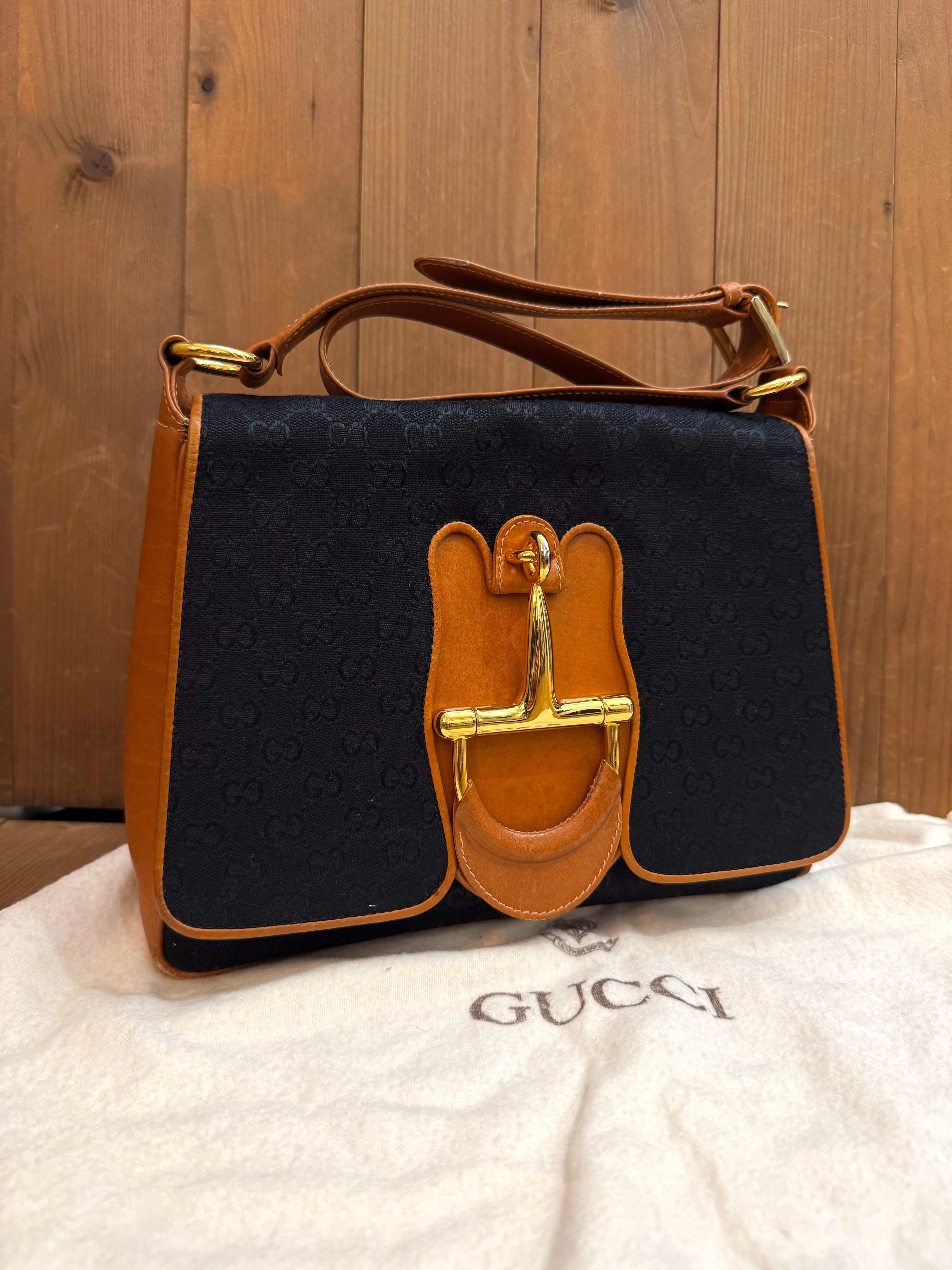 Este bolso bandolera GUCCI Vintage está confeccionado en jacquard con el monograma GG en negro, ribeteado en suave piel de ternero marrón y con un enorme bocado de caballo en la parte delantera. El cierre frontal con solapa se abre a un interior de