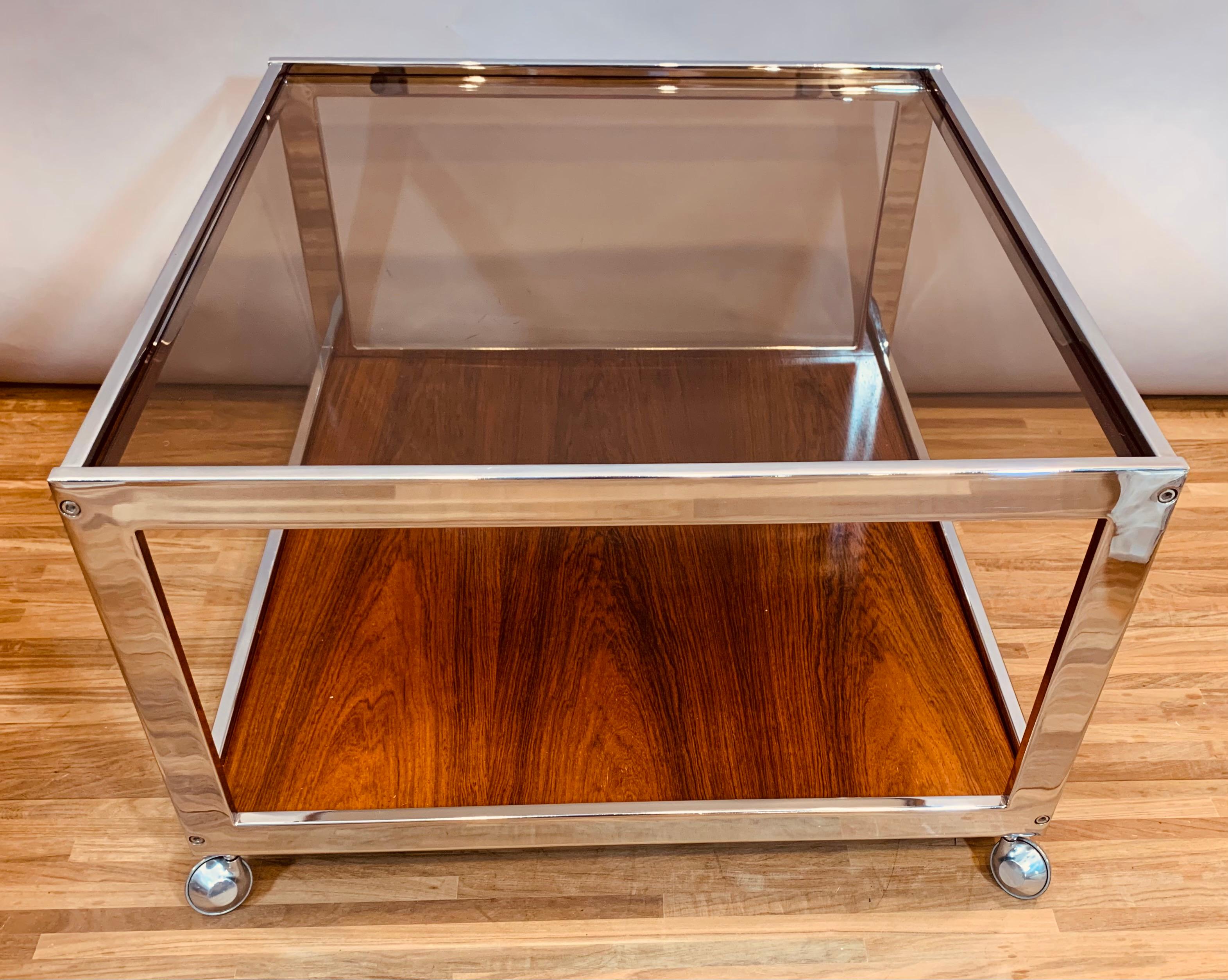 A vintage smoked glass, chromed metal and Rosewood veneer square coffee table. Designed in the 1970s by British designer Howard Miller for MDA - Miller Design Associates.

The square coffee table features features a thick smoked glass top which