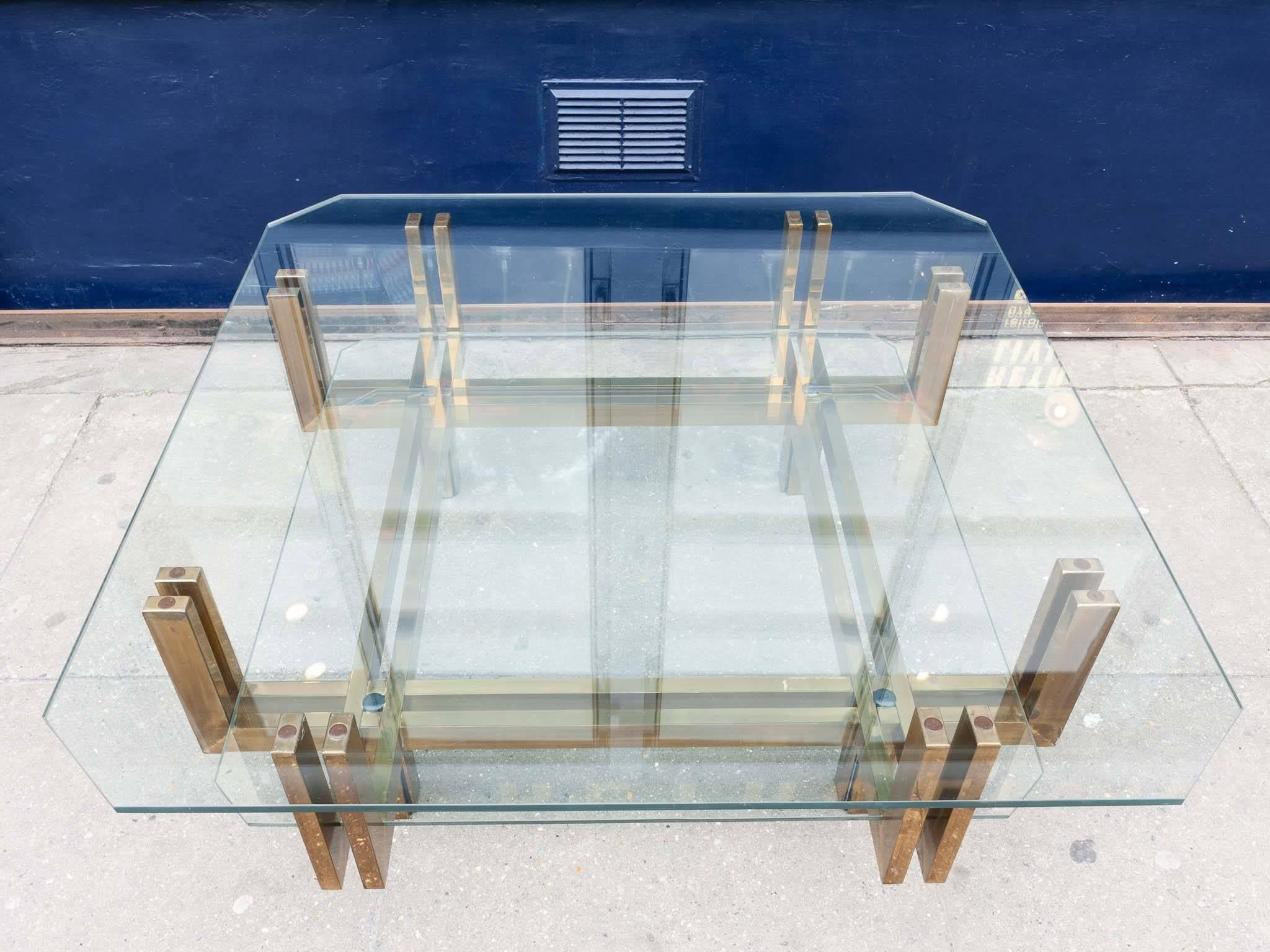 1970s chic and glamorous vintage brass and glass frameless coffee table in the style of Romeo Rega. The table has two floating glass shelves with the lower shelf sitting inside of the outer two pronged supporting base. The brass base has a wonderful