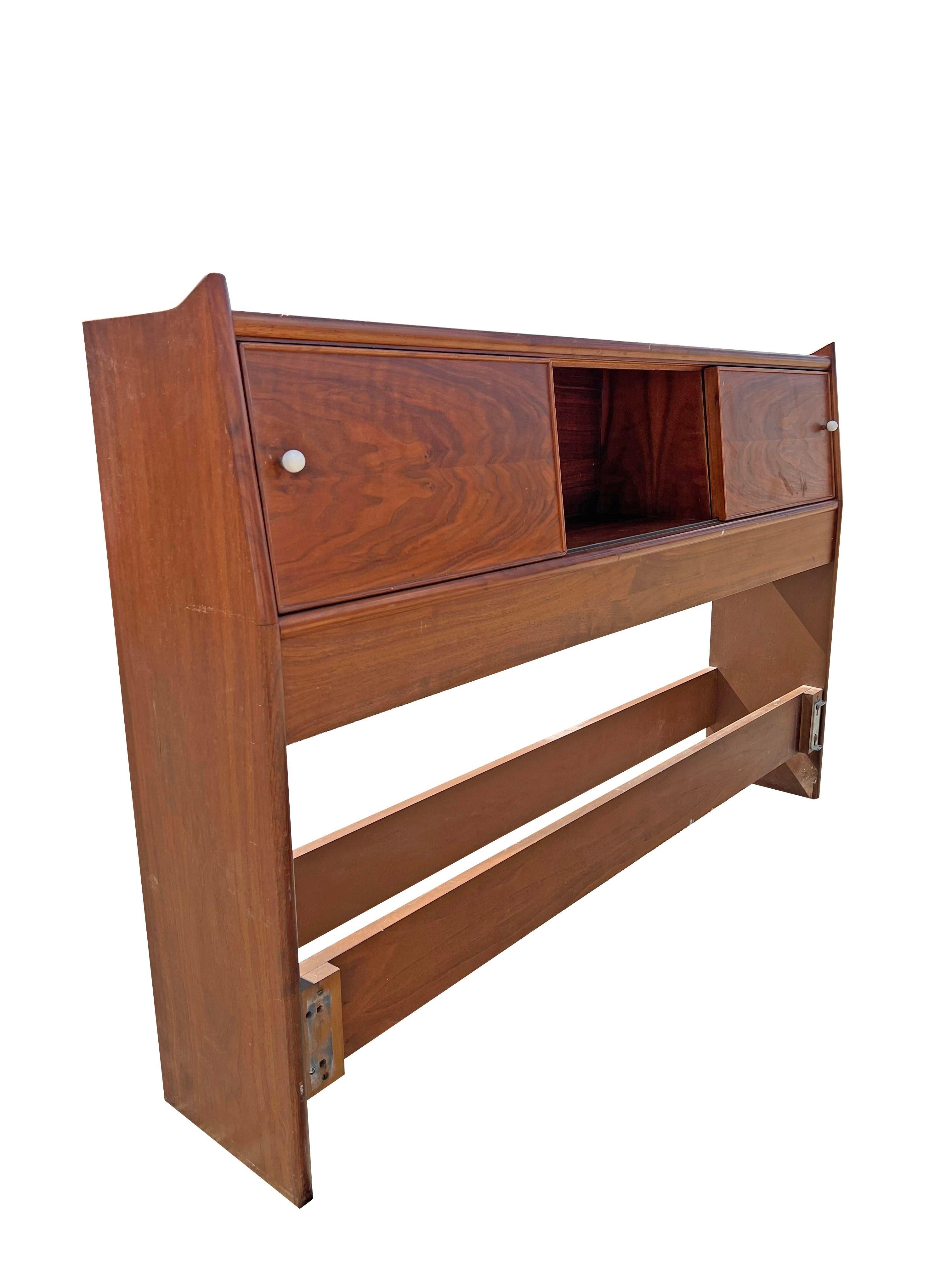 This vintage full-size headboard, designed by Kipp Stewart for Drexel, showcases the iconic Declaration style. The headboard's sliding doors offer not only a sleek aesthetic but also practical storage solutions, revealing hidden compartments that