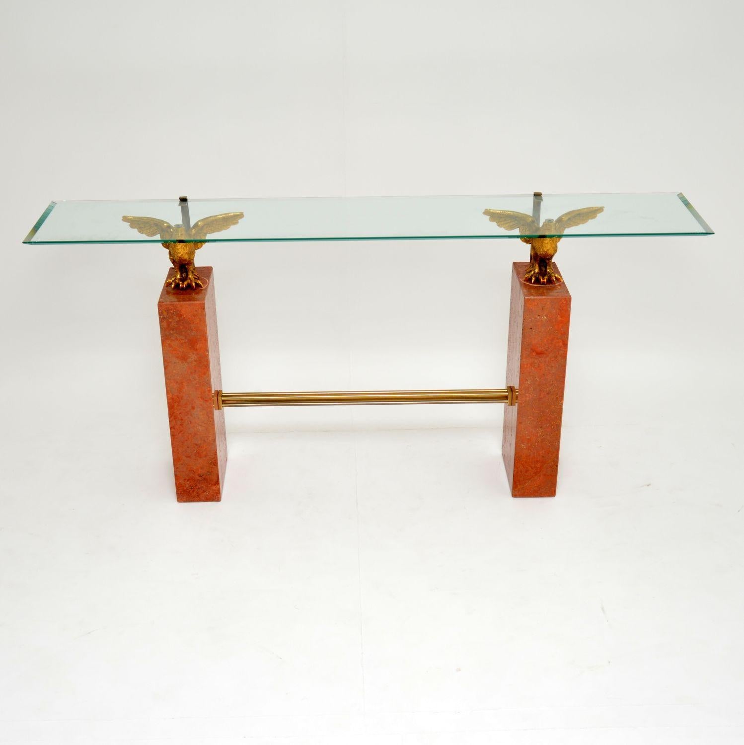 A stunning vintage console table, comprised of two solid marble pedestals, with brass fixtures and a bevelled glass top. The top is supported by solid brass eagles, this piece of furniture is superb quality all round. The condition is excellent for
