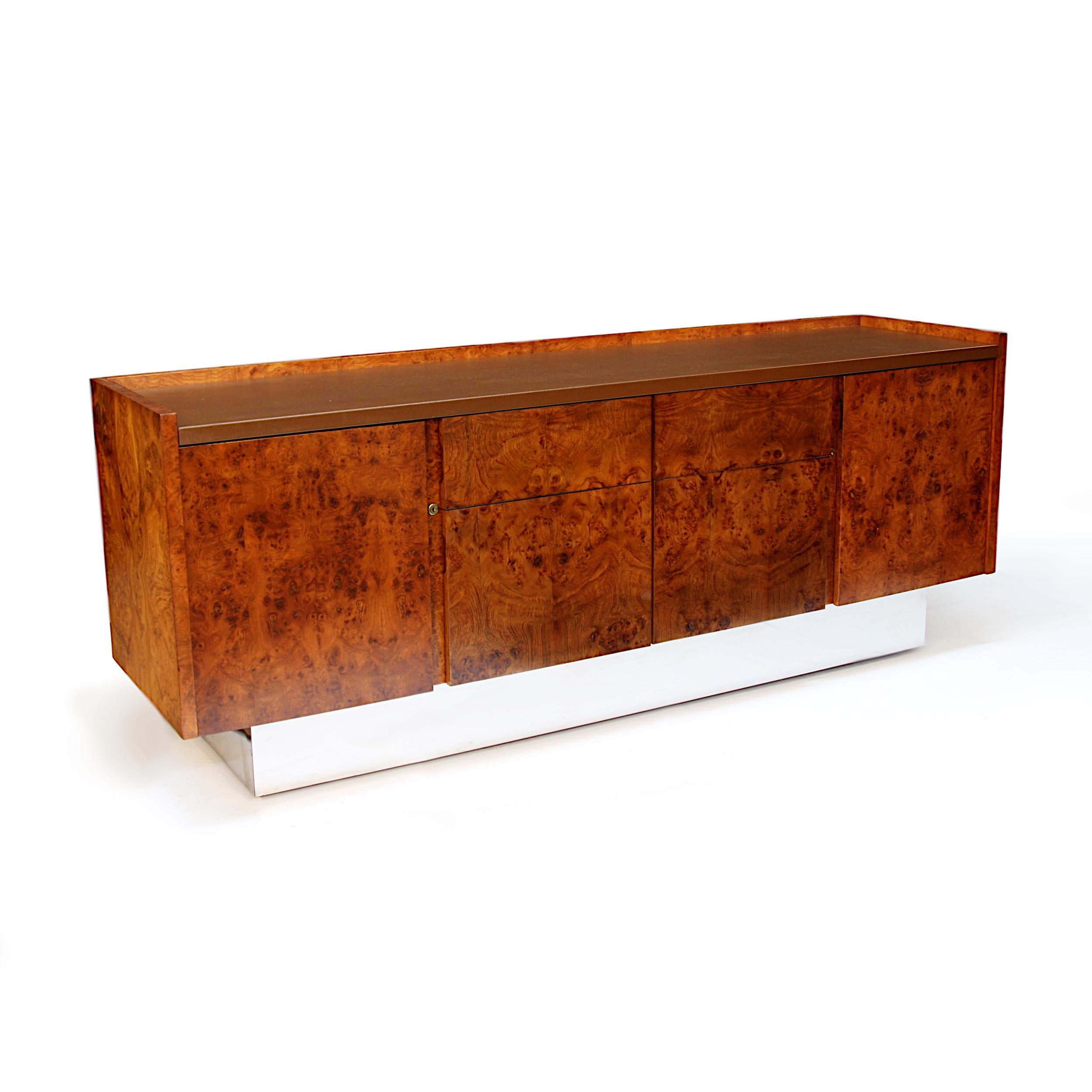 Amazing 1970s executive credenza by Biltrite Furniture Mfg Inc of Montreal, Canada. This sleek, slab-sided, sideboard features gorgeous, book-matched olivewood veneer, Leather writing surface, chrome pedestal base, and a unique Minimalist design