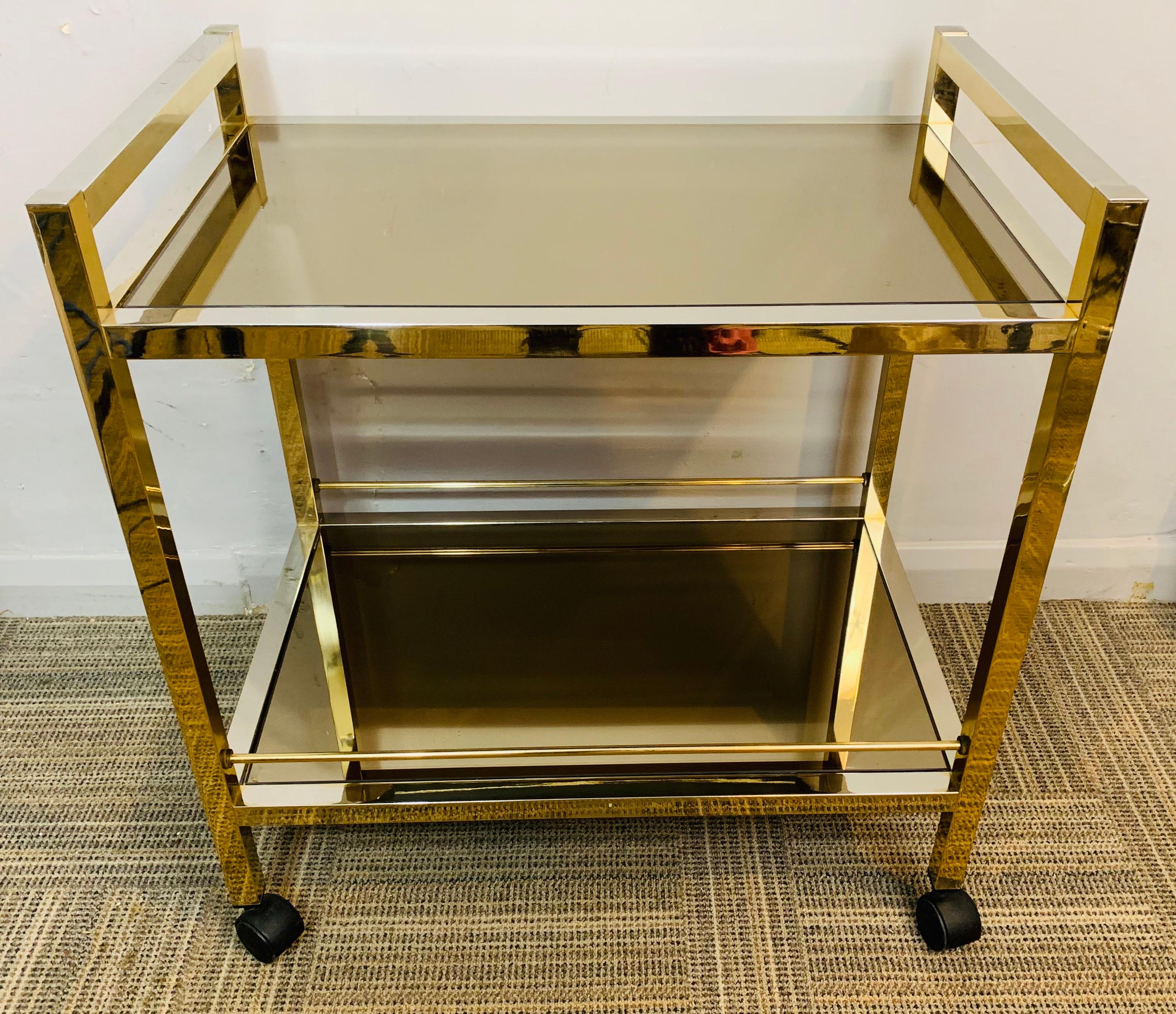 1970s Italian, modernist, brassed-chrome with mirrored smoked-glass shelves drinks trolley or bar cart. The rectangular trolley is constructed with a brassed-chrome metal frame and smoked mirrored glass shelves on black plastic castor wheels. The