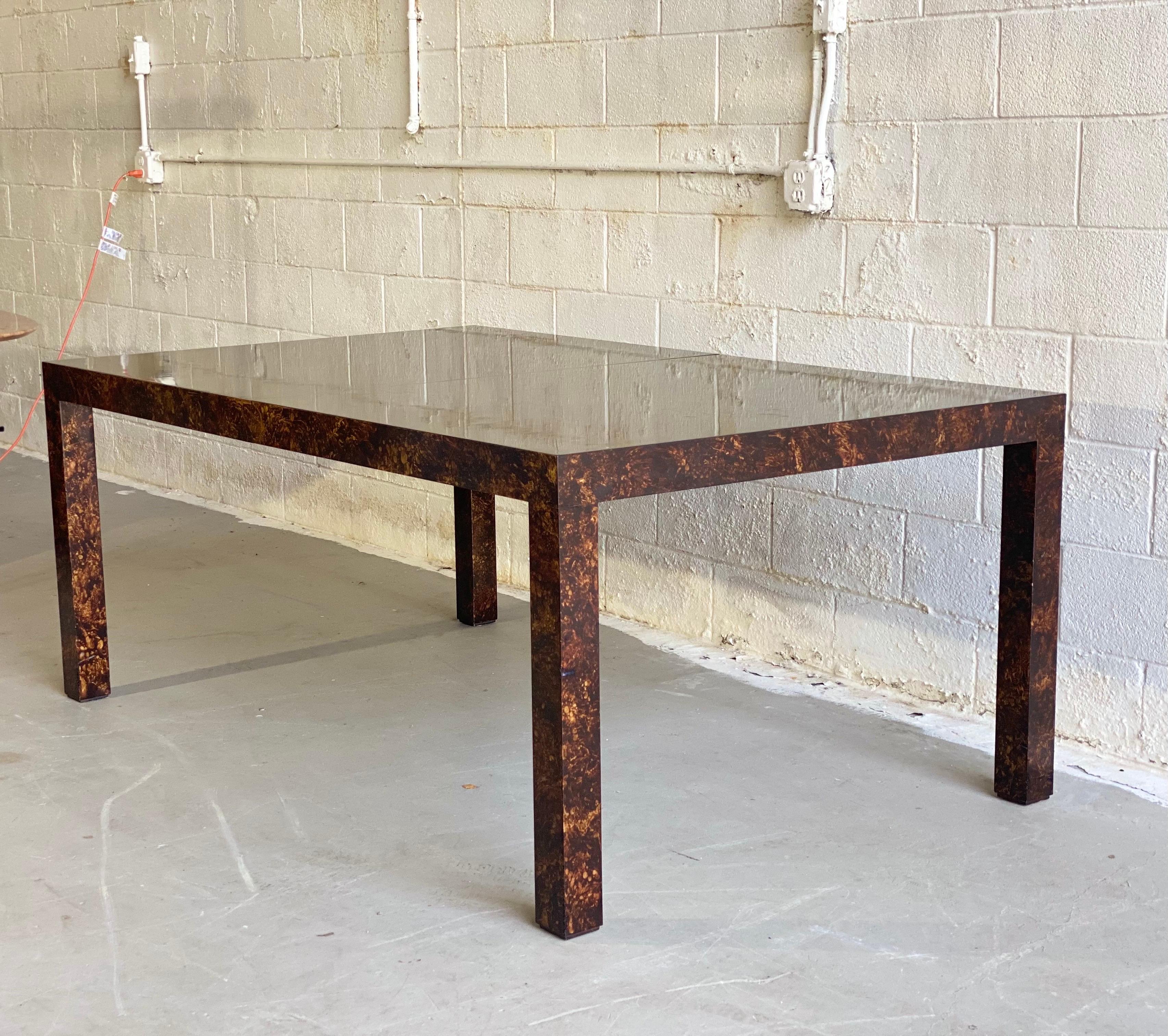 We are very pleased to offer a chic, parsons dining table, circa the 1970s. This beautiful expanding table showcases a lacquered oil drop technique that creates an exquisite faux tortoiseshell finish. Perfect for entertaining flexibility, this table
