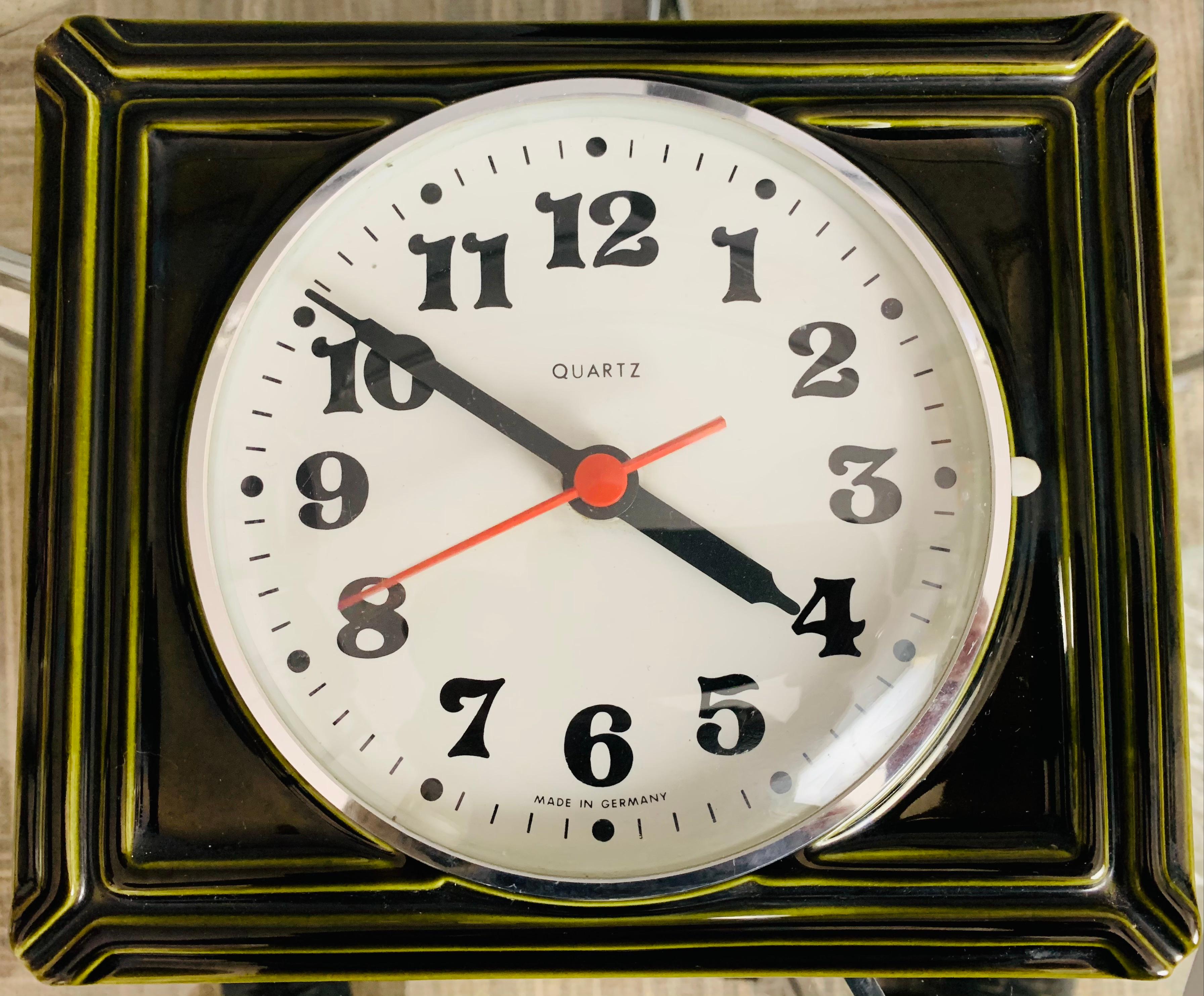 A vintage, 1970s, German Quartz green ceramic rectangular wall clock with a white clock face and black numerals. The clock face is protected with a plastic cover and silver surround which opens to the right. The hands are black and the second hand