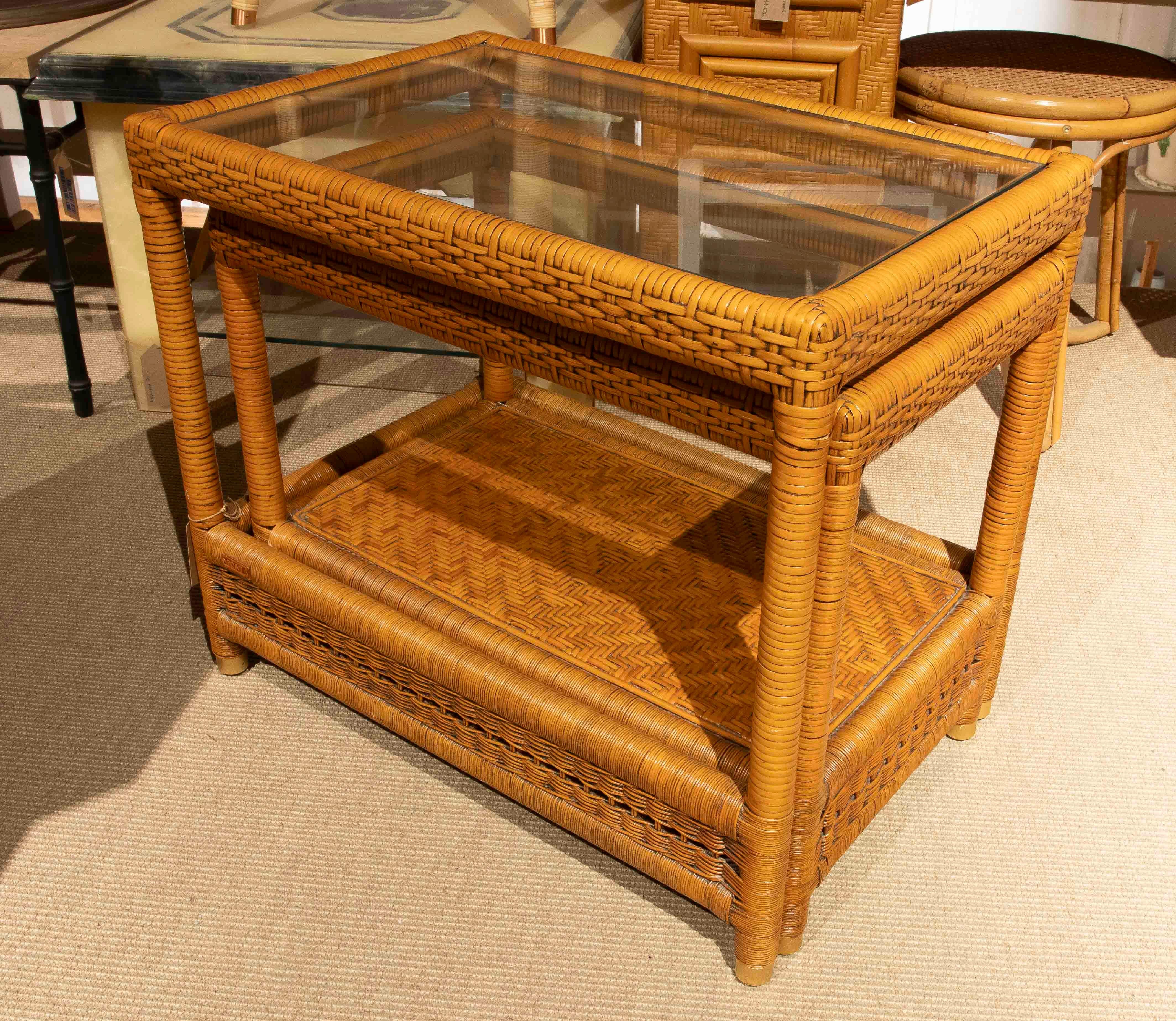 Un ensemble d'élégantes tables gigognes vintage fabriquées en rotin tressé avec des plateaux en verre. Cet ensemble de deux tables emboîtables combine fonctionnalité et style, offrant des solutions polyvalentes pour les salons, les patios ou les