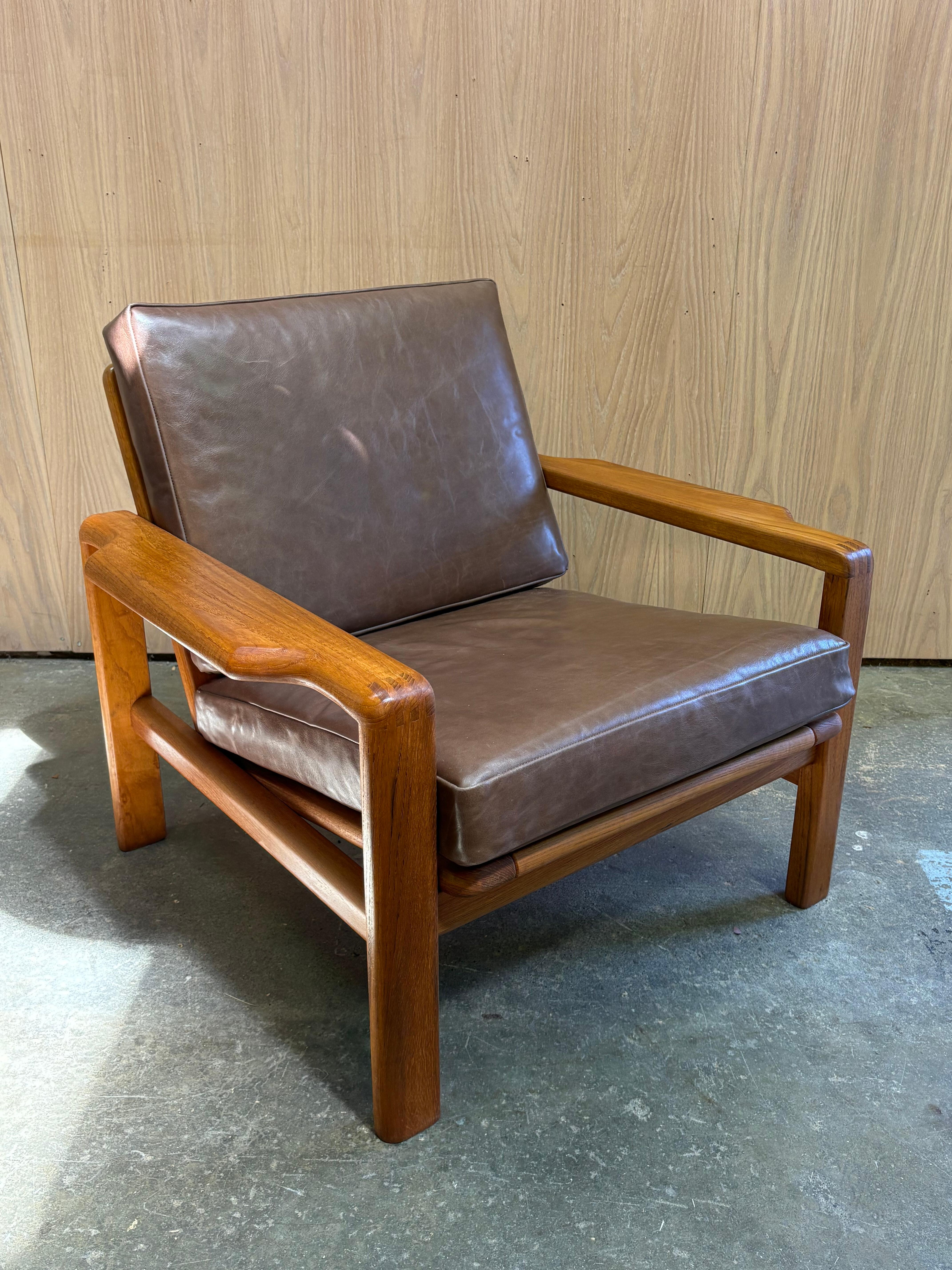 Elegante expresión de la artesanía y la forma de los años setenta, este sillón de teca maciza tiene unos atrevidos brazos en forma de pala con uniones de dedos a la vista y una postura baja y segura. El asiento ancho y el respaldo relajado ofrecen