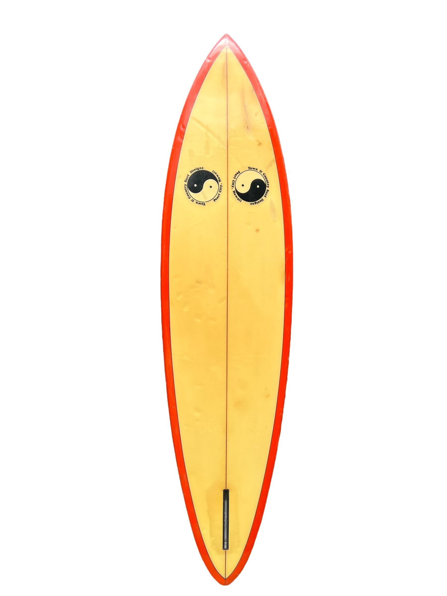 planche de surf Town & Country 1979 fabriquée par Ed Angulo. Il est doté d'un magnifique pont/rails teintés en rouge, de doubles laminés T&C et d'un aileron simple en forme de boîte. Un exemple remarquable d'une planche de surf des années 1970