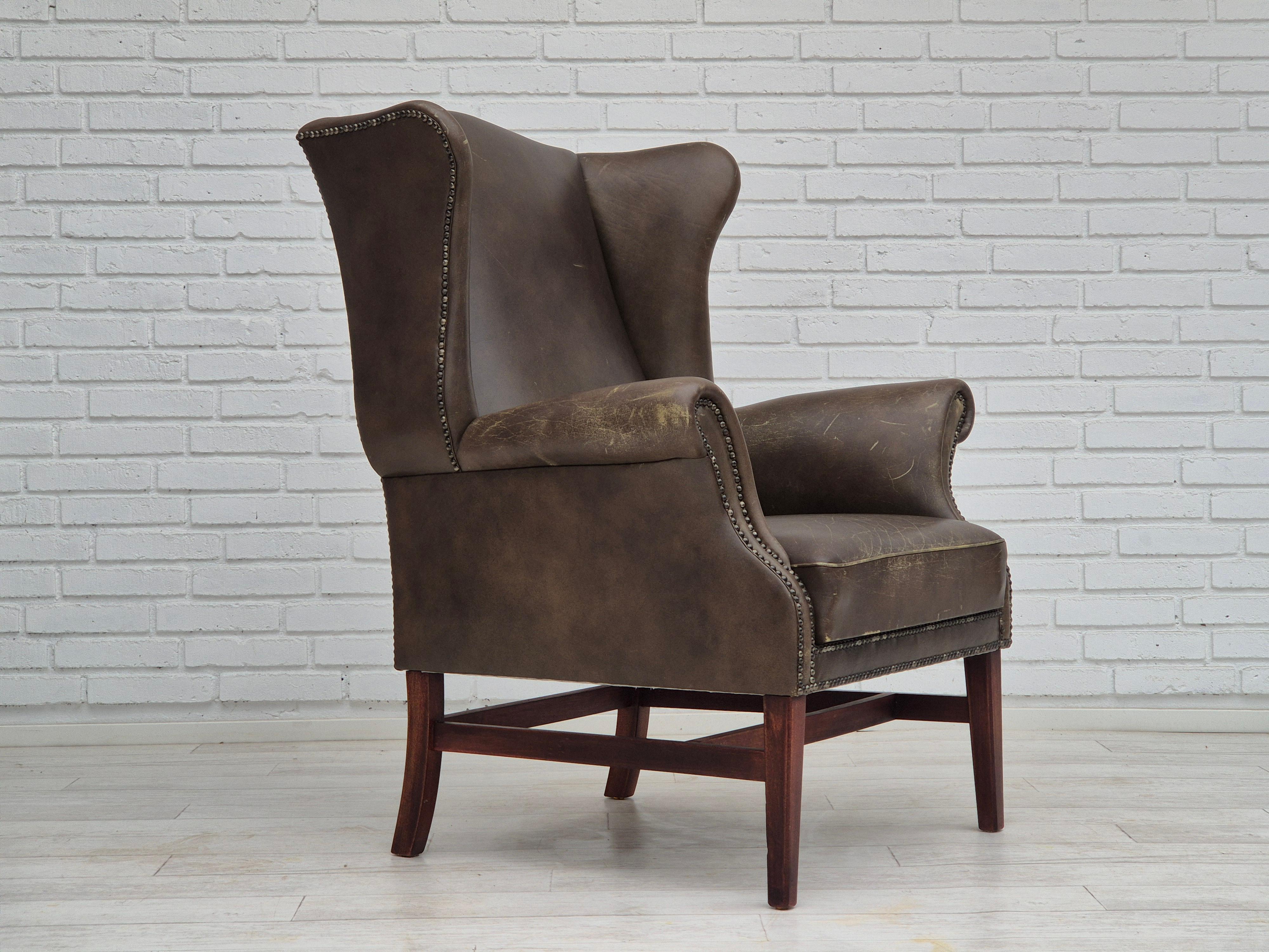 1970s, vintage wingback armchair in original good condition: no smells and no stains. Patinated brown leather. Beech wood legs. Springs in the seat. Manufactured by Danish or Swedish furniture maker in about 1975-79s.