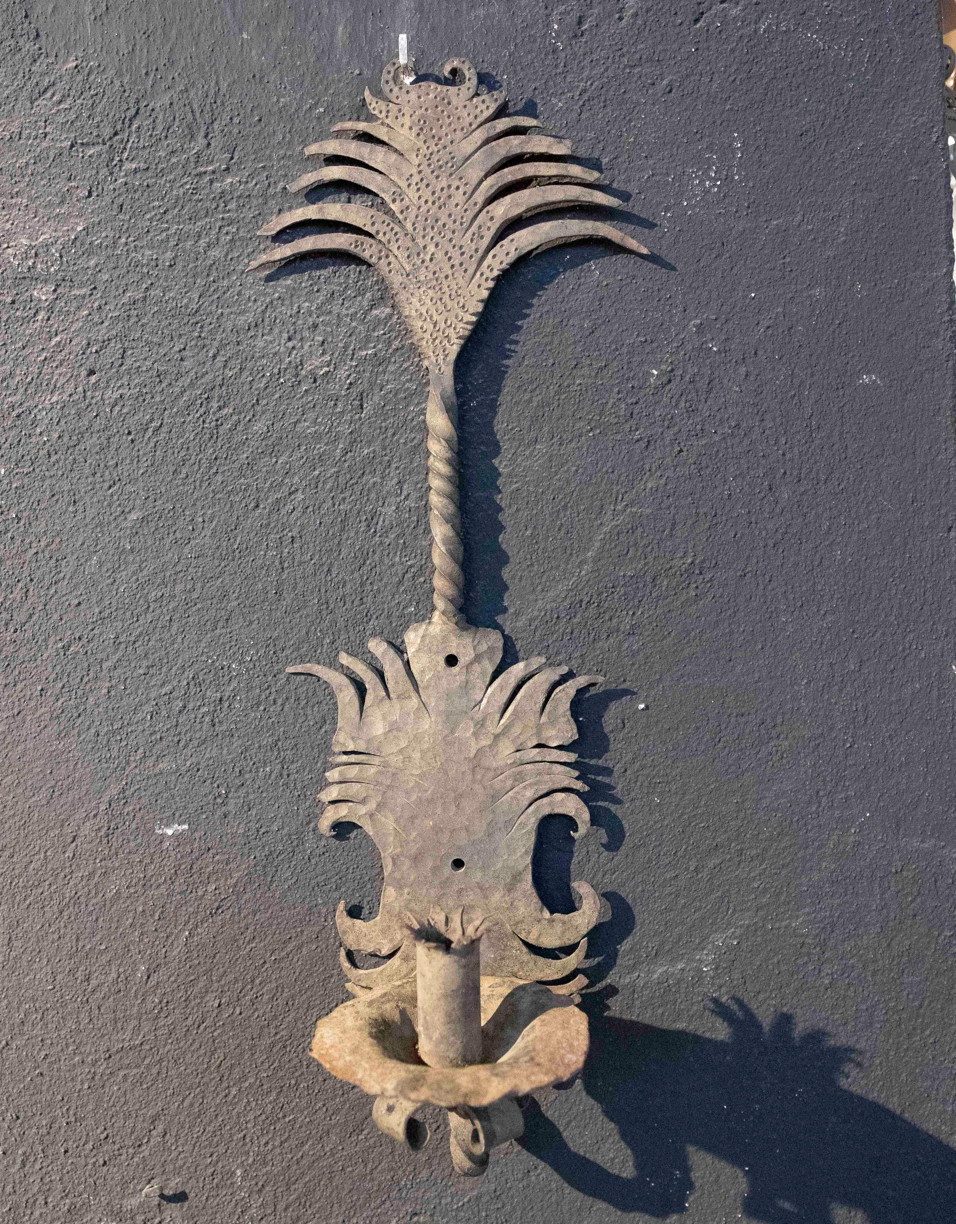 Auténtico aplique de hierro forjado, con un diseño que destaca por su estilo artesanal y detalles decorativos inspirados en motivos naturales. La pieza presenta formas onduladas y una textura única que evoca hojas y elementos orgánicos, añadiendo un
