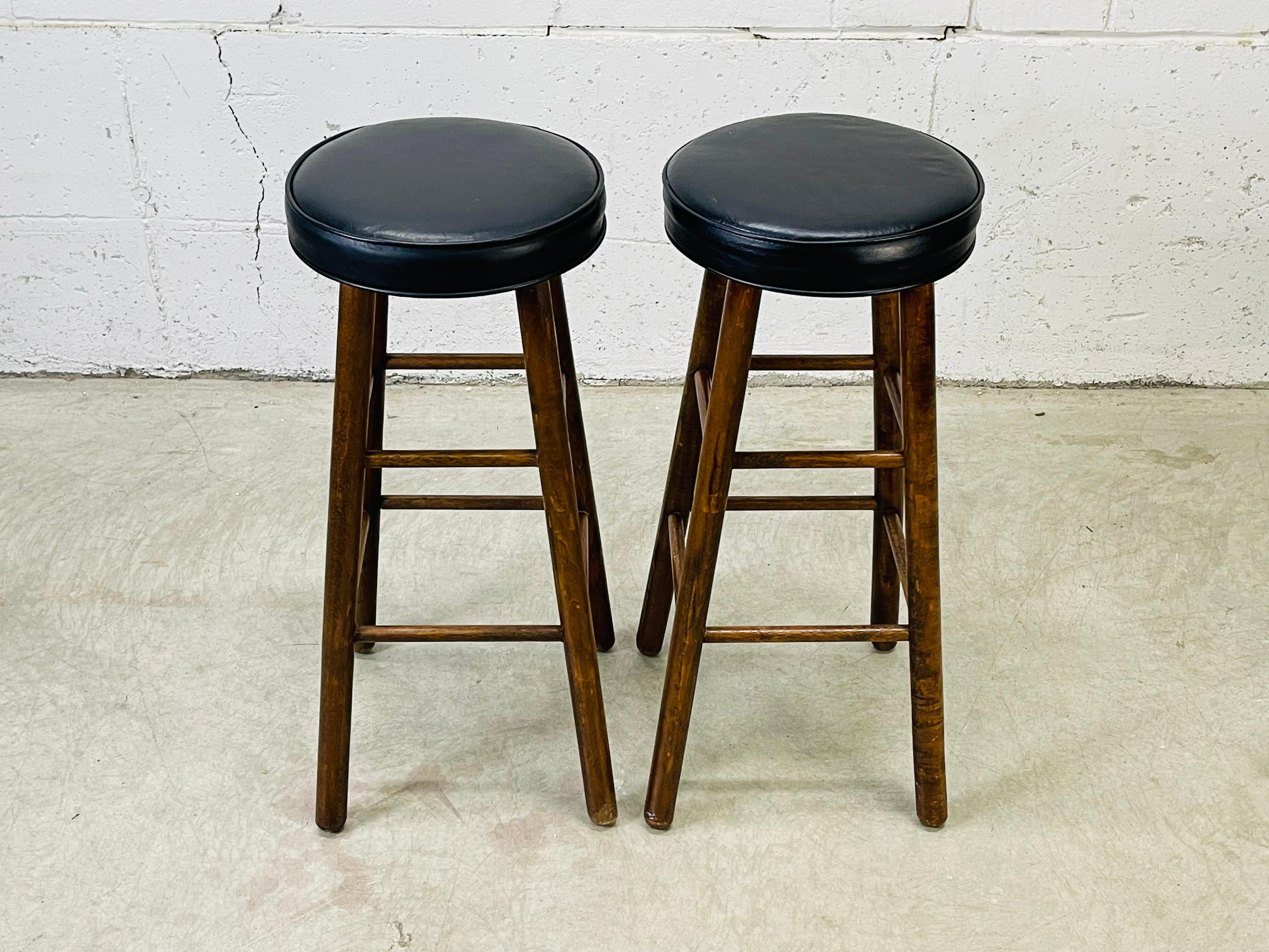 Vintage 1970s pair of round black vinyl top bar stools with wood bases. The stools are solid and sturdy. Marked.