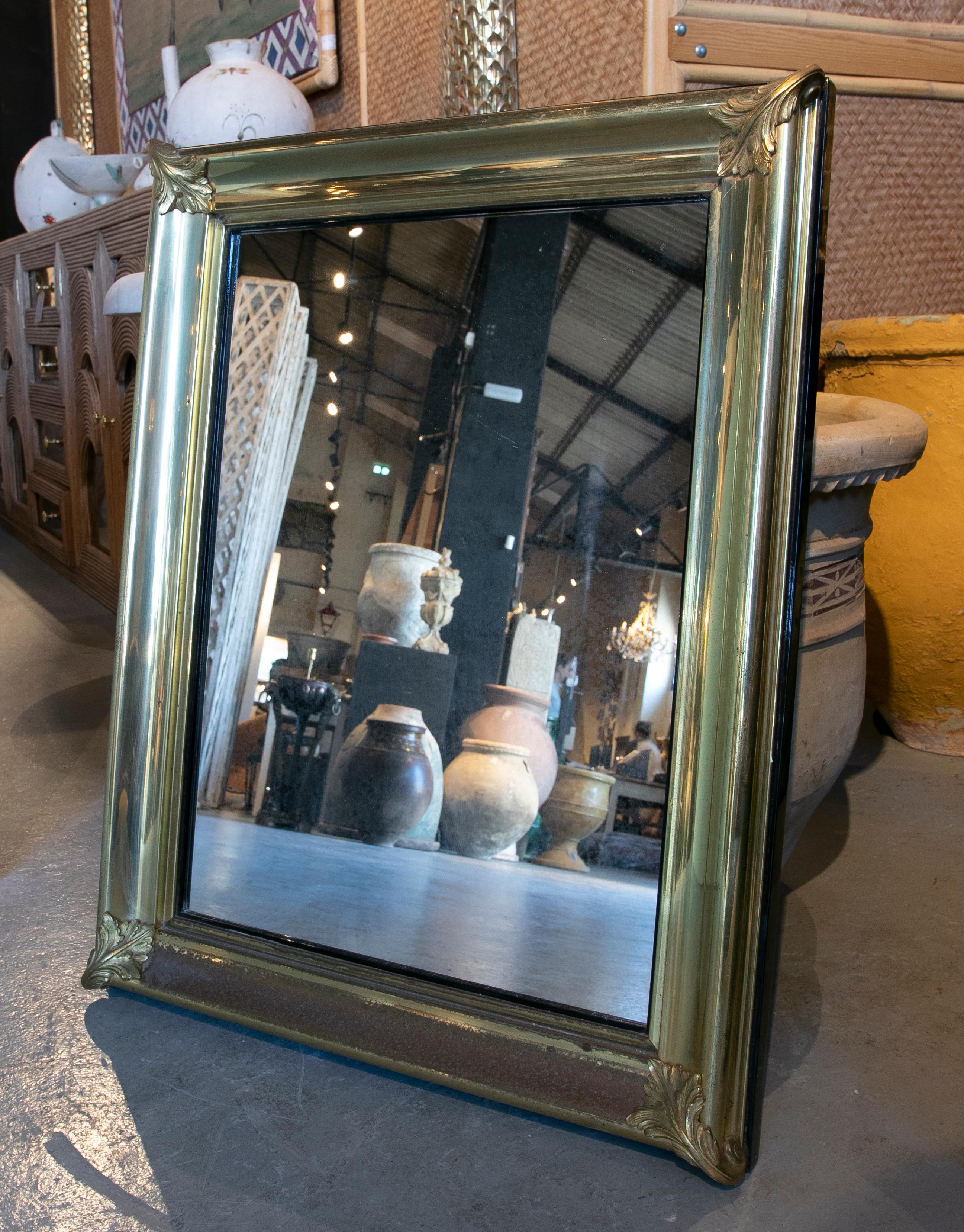 1970s Wall mirror made of metal and bronze. It has a wide frame with ornaments in the corners; plus said frame has a golden patina.