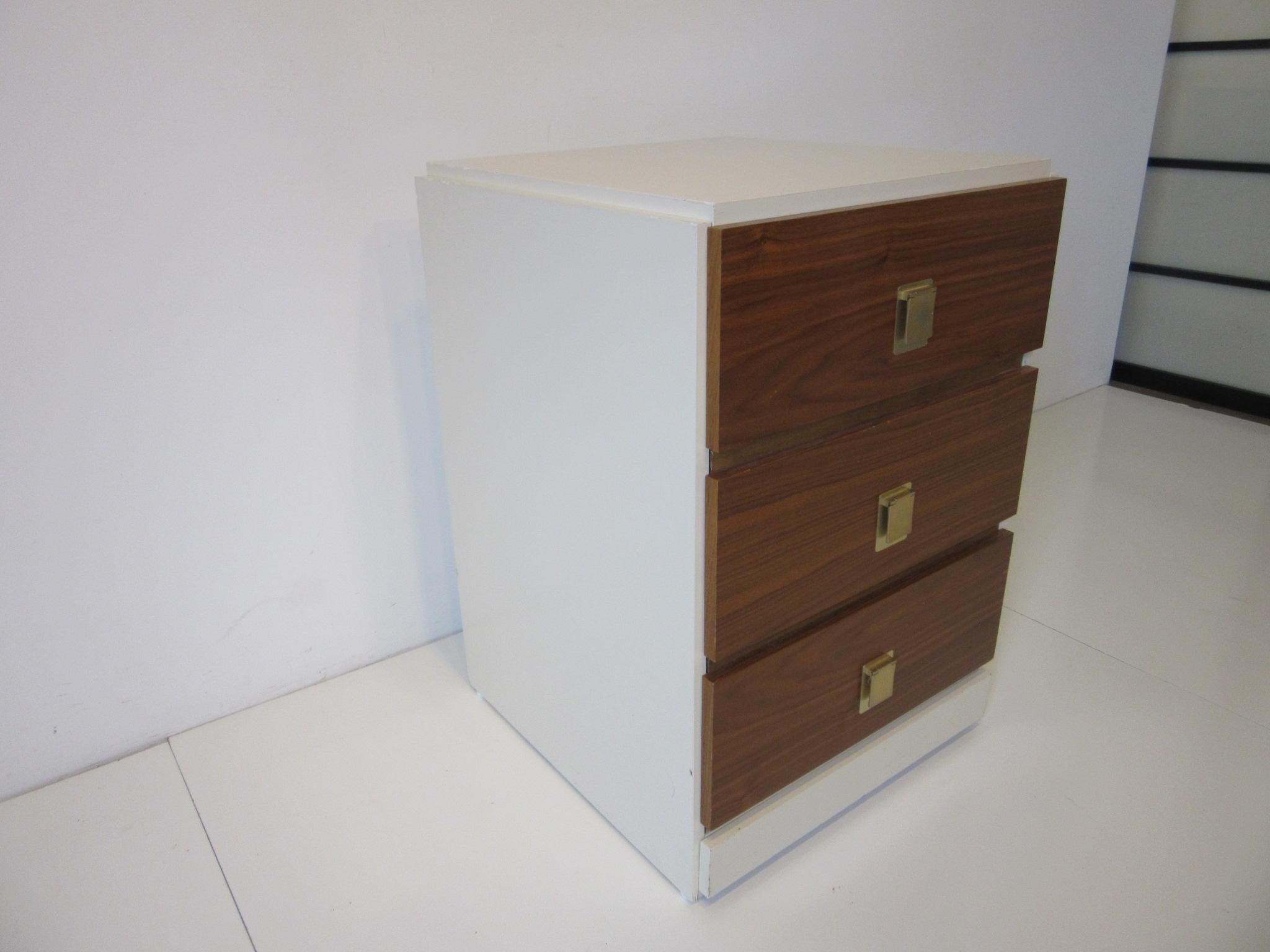 A small three-drawer chest with walnut drawer fronts having brass pulls and a cream lacquer painted cabinet in the style of Milo Baughman manufactured in Canada. Can be used as a single nightstand or where you need some storage in a small space.