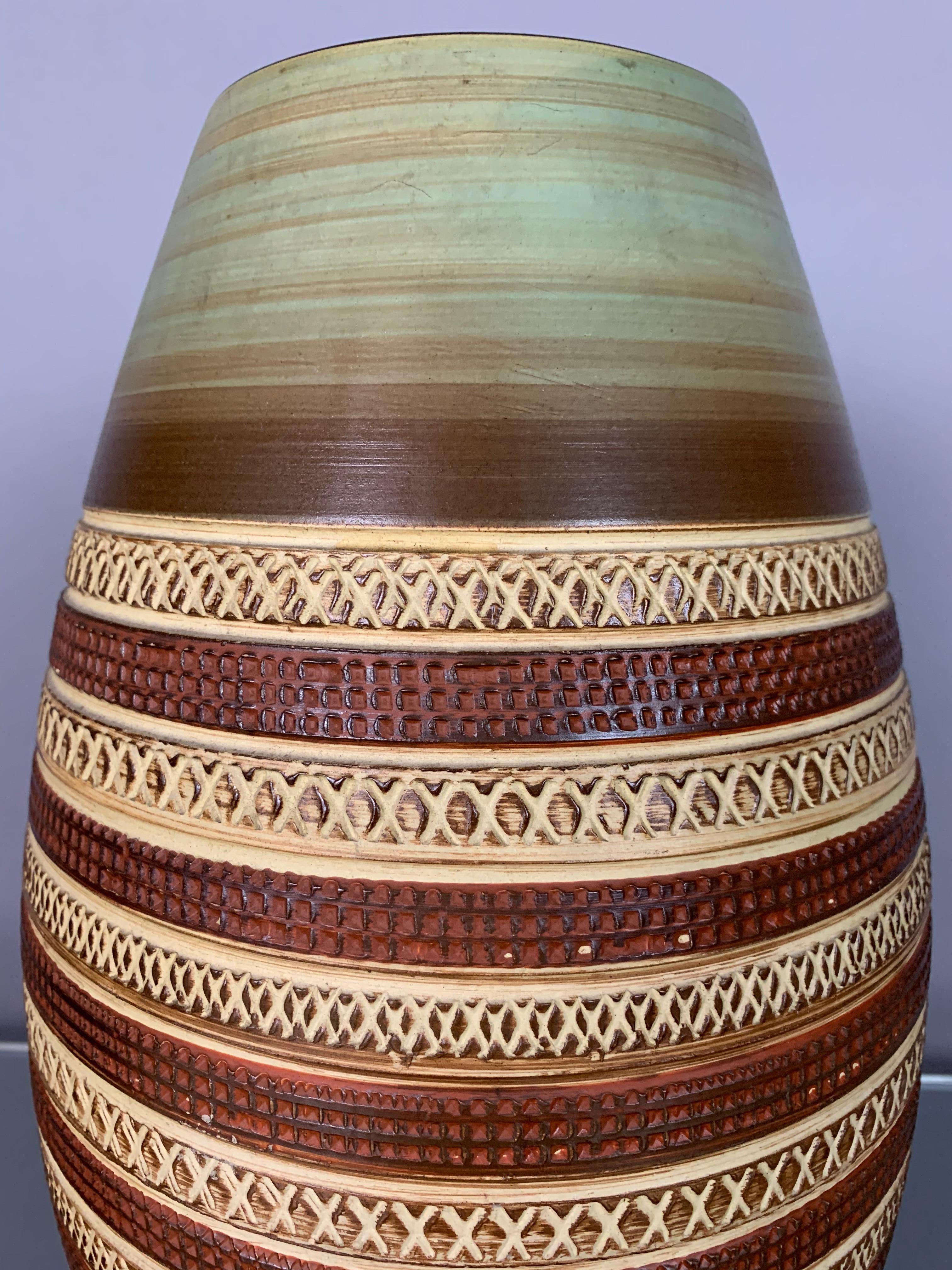 A large West German pottery vase with an interesting, painted, indented, design which runs in horizontal hoops around the outside of the vase. The vase has been painted in autumnal colors of green at the top and bottom and alternating light and dark
