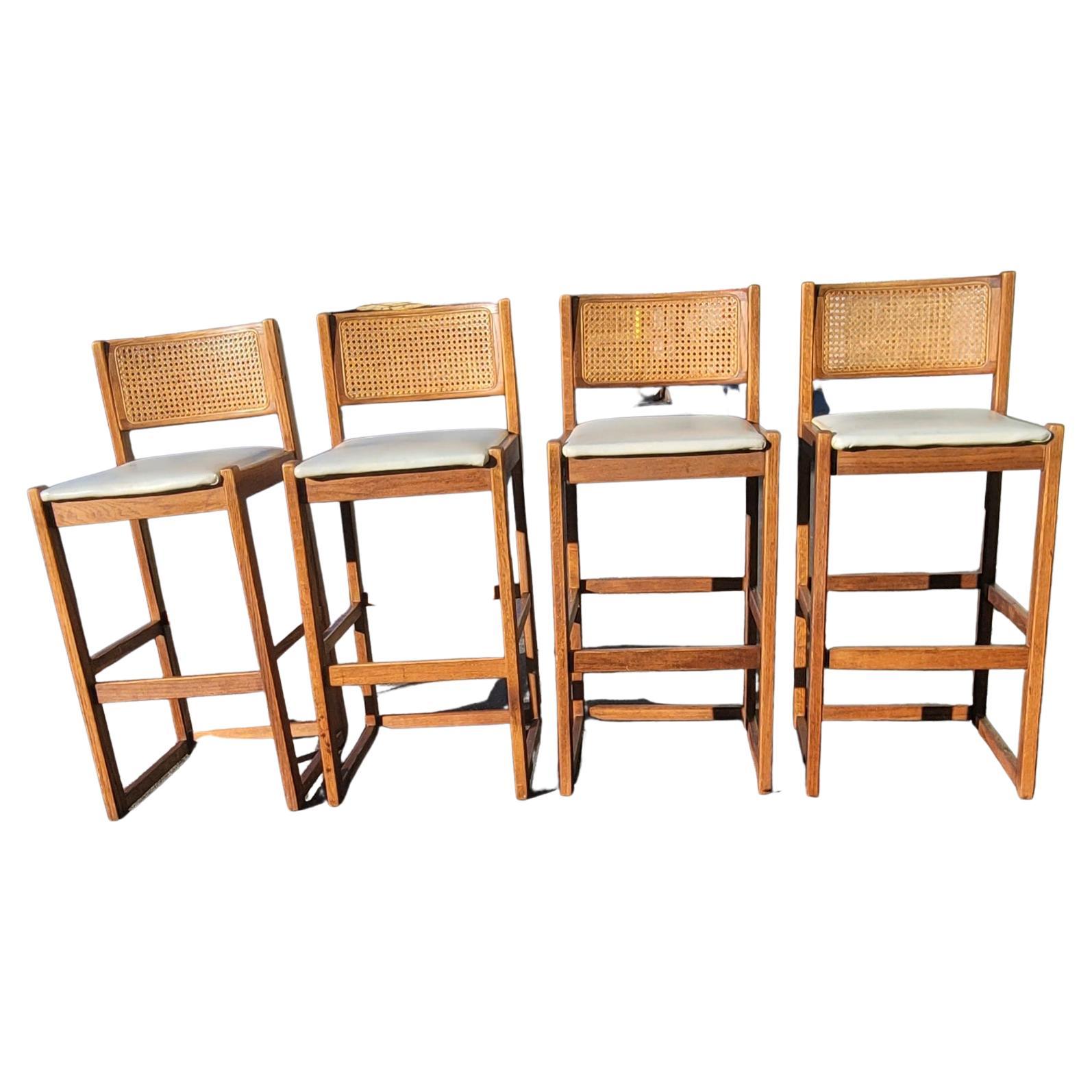 A set four (4) 1970s Whitaker Furniture Oak and Cane Back with Leatherette Seat Bar Stools in good vintage condition. Measure 17