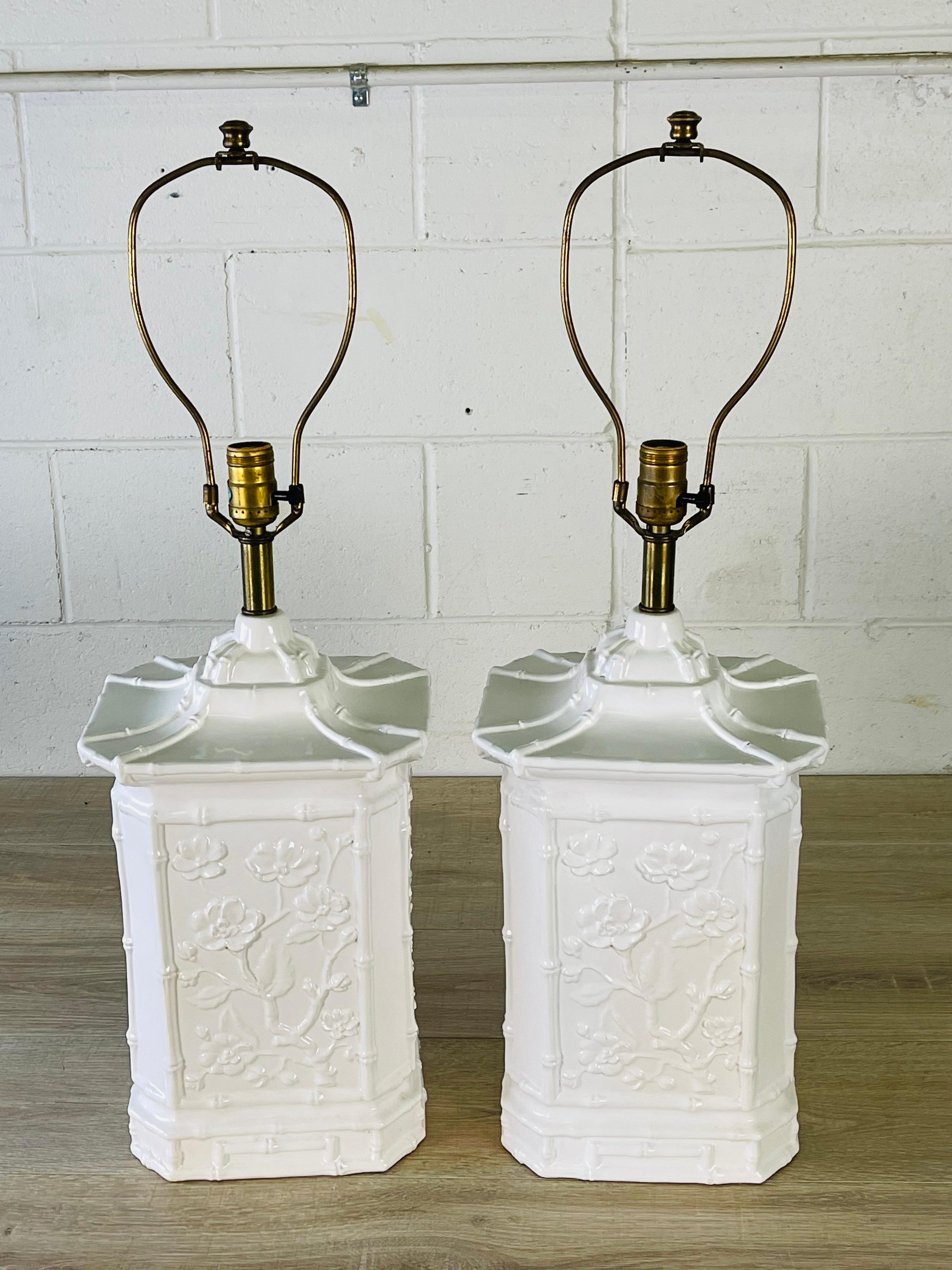 Vintage 1970s Asian style ceramic table lamps in white. The lamps have a floral and bamboo design on all sides of the lamps. Wired for the US and in working condition. Uses a standard 3-way bulb. Socket, 20.5” height. Harp, 6” diameter x 9” height.