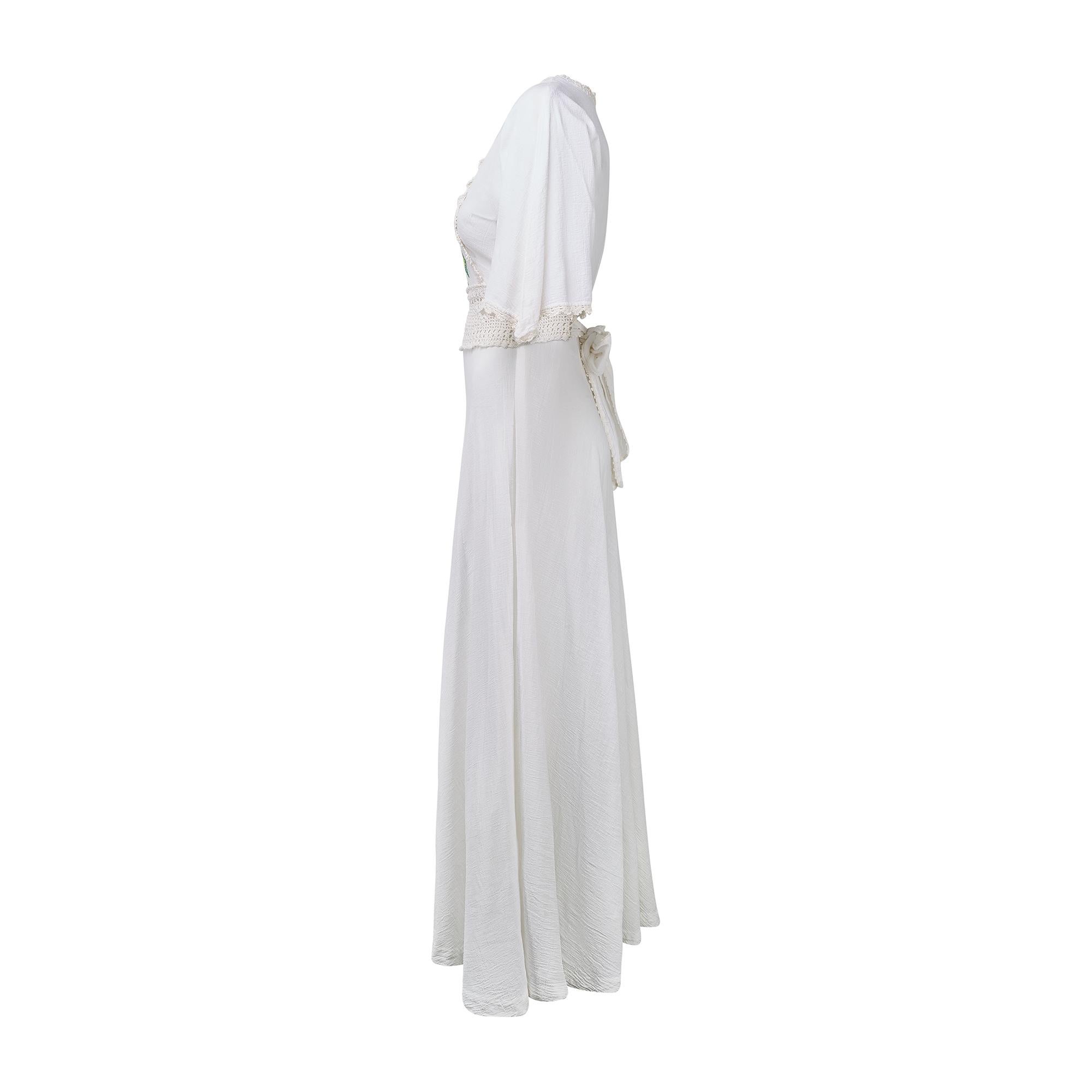 This 1970s maxi-dress is crafted from rich white cheesecloth.  It has elbow-length, fluttering sleeves and falls to the ankle. The dress is trimmed with off-white crochet around the neckline, cuffs and bust and a thicker band of crochet around the
