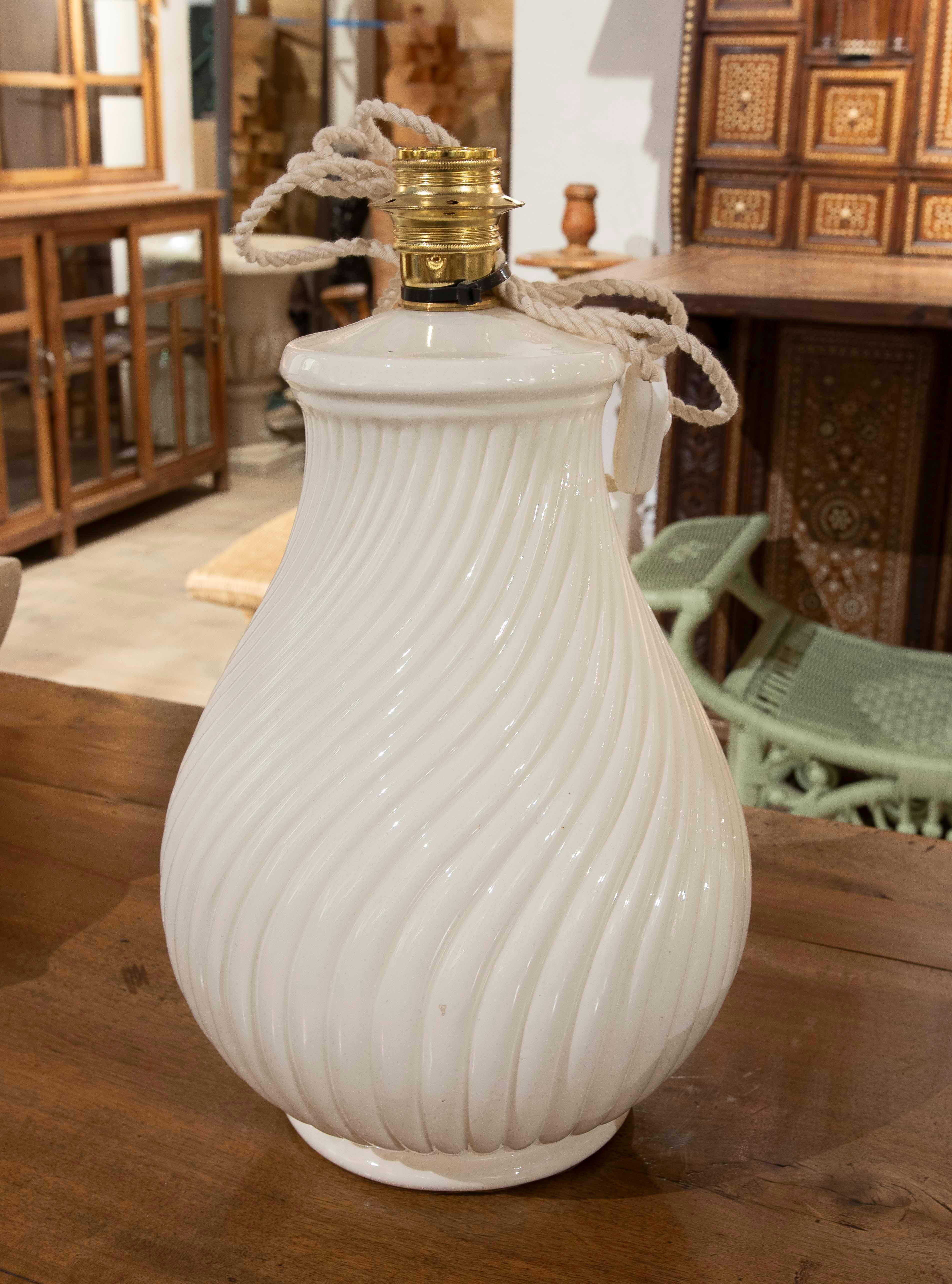 Élégante lampe de table avec une base en céramique blanche et un design raffiné à nervures en spirale, qui apporte une touche sophistiquée et intemporelle. Sa structure volumineuse et stylisée en fait une pièce idéale pour tous les espaces, qu'ils
