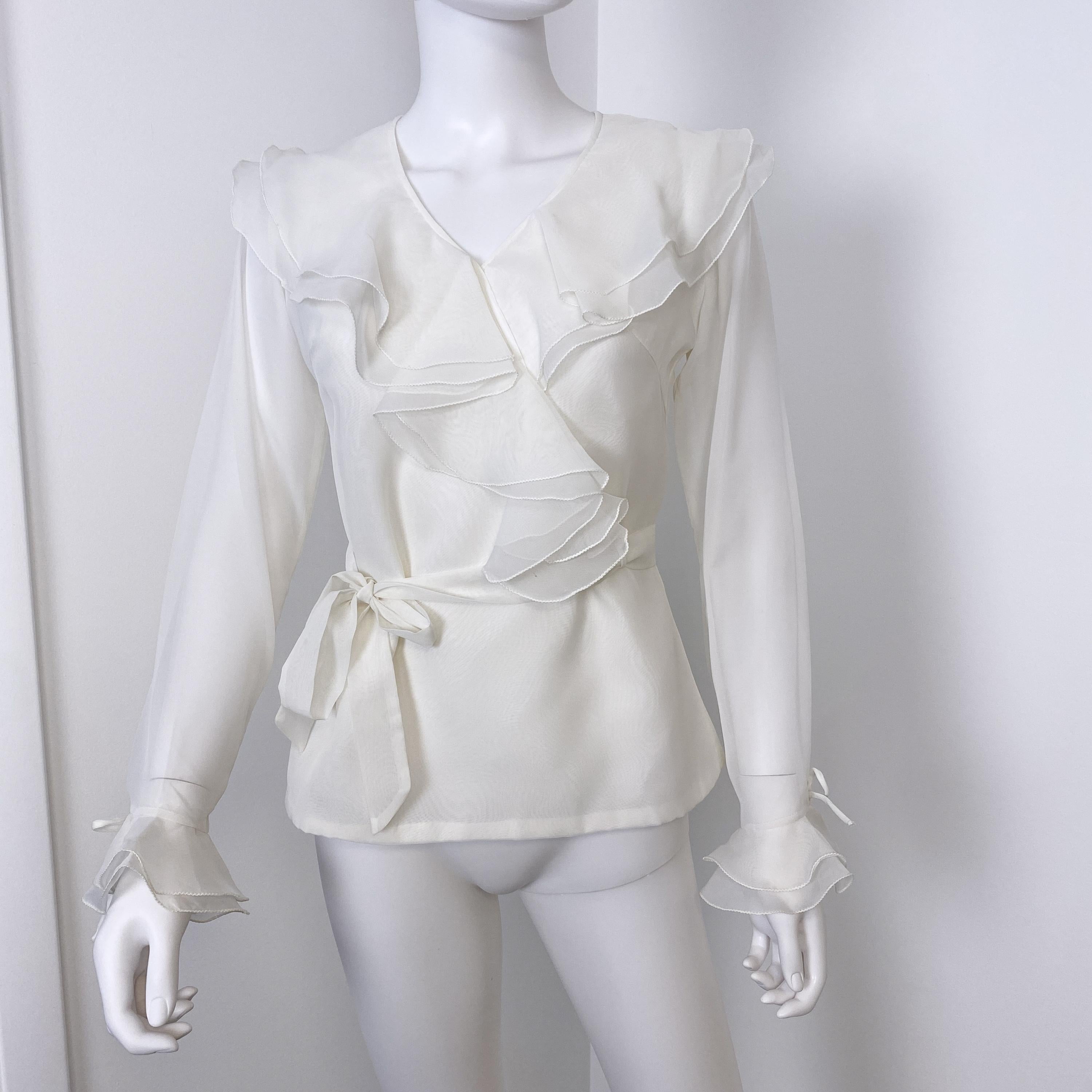 This is an outstanding organdy and sheer blouse tunic from the 1970s. The composition is very vaporous, with sheer sleeves finished with a link and double ruffles. The V-shaped front without a collar is decorated with two rows of ruffles and is