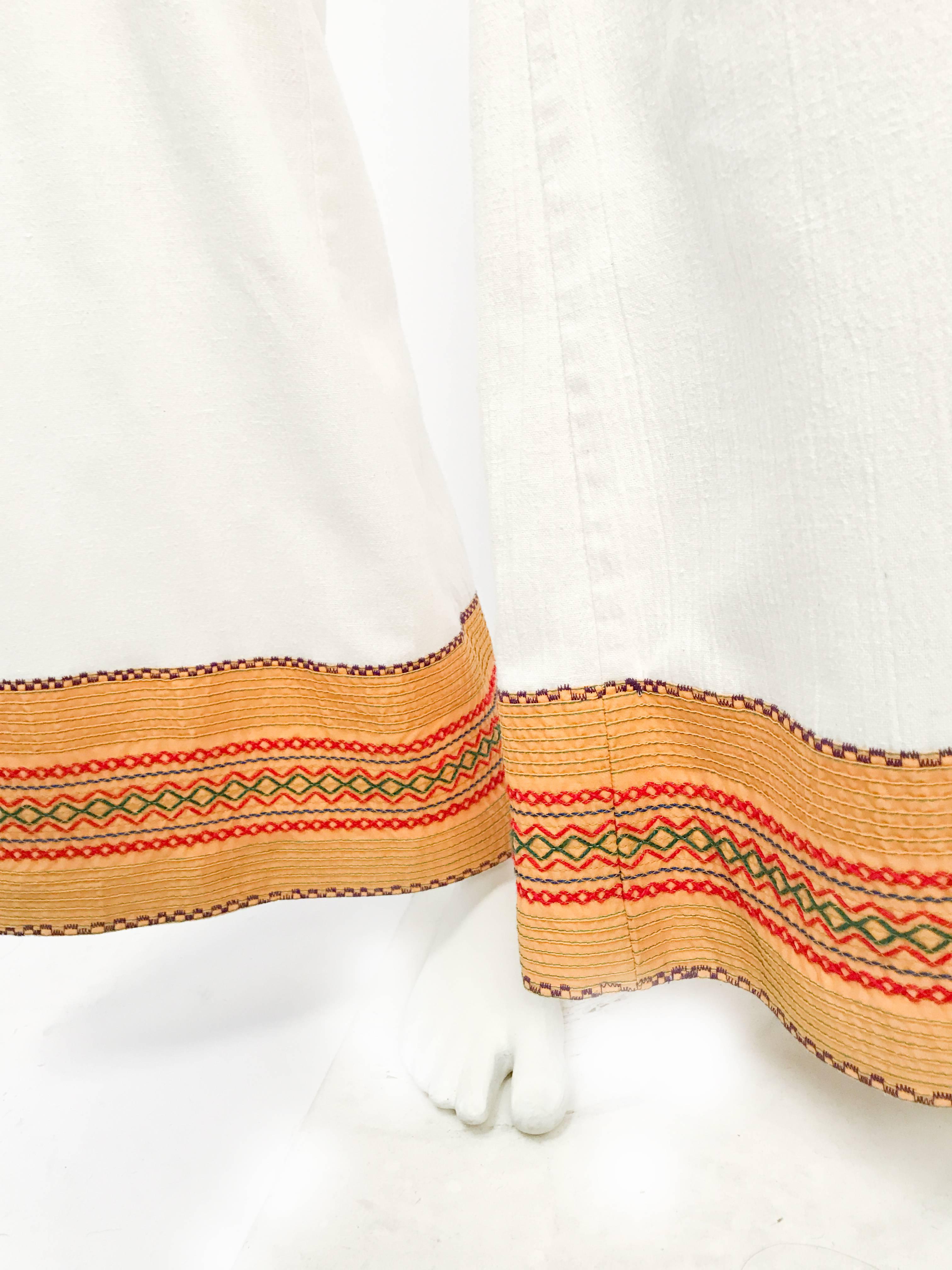 1970s White Wide Legged Pants with Embellished Hems. White wide-legged pants with yellow/red/green embroidered hems and zipper/button closure.