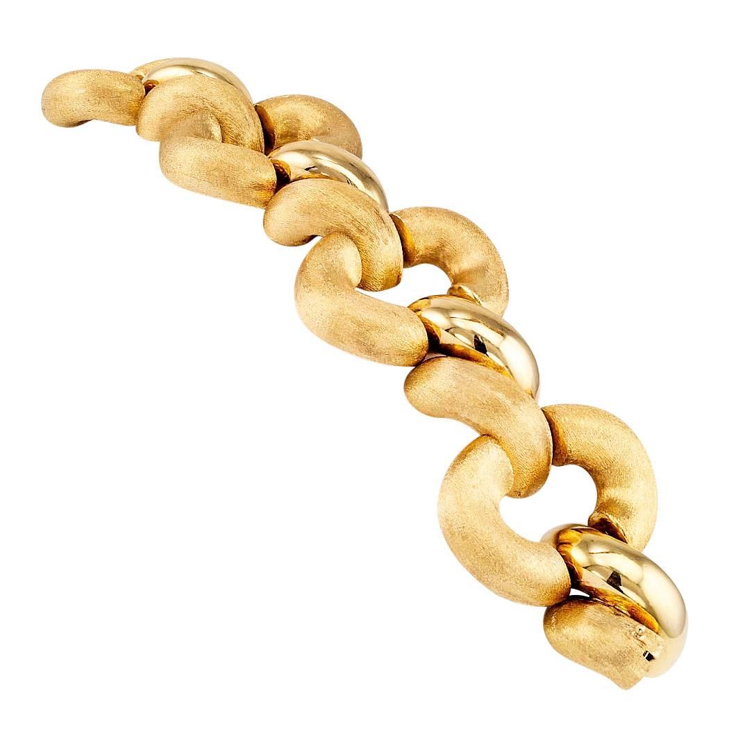 1980s gold link bracelet. The extra wide 18-karat gold link bracelet is designed as a series of massive tubular, oval gold links decorated by a Florentine texture with double connectors alternating between a similar texture and bright polished